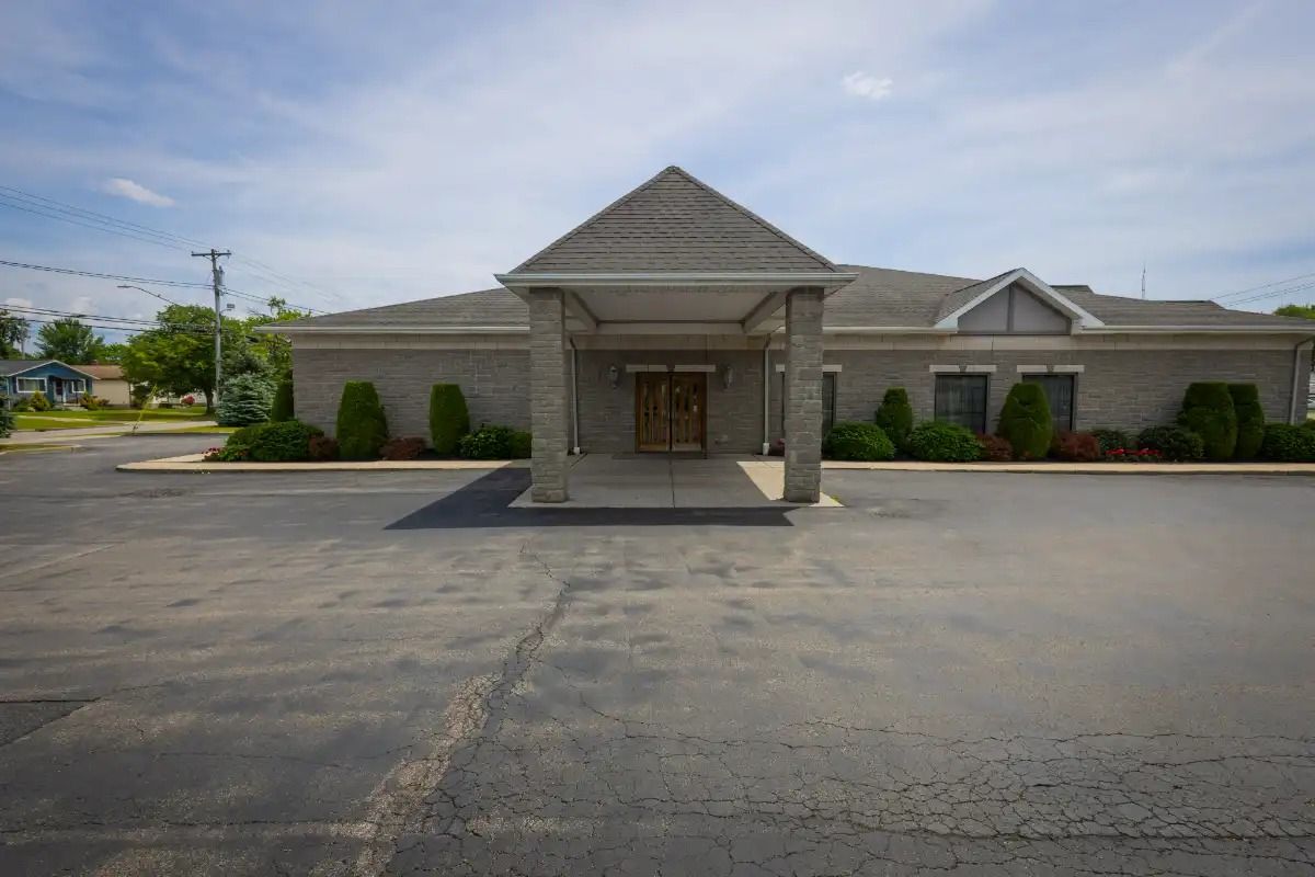 Gray brick building with covered entrance and asphalt parking lot.