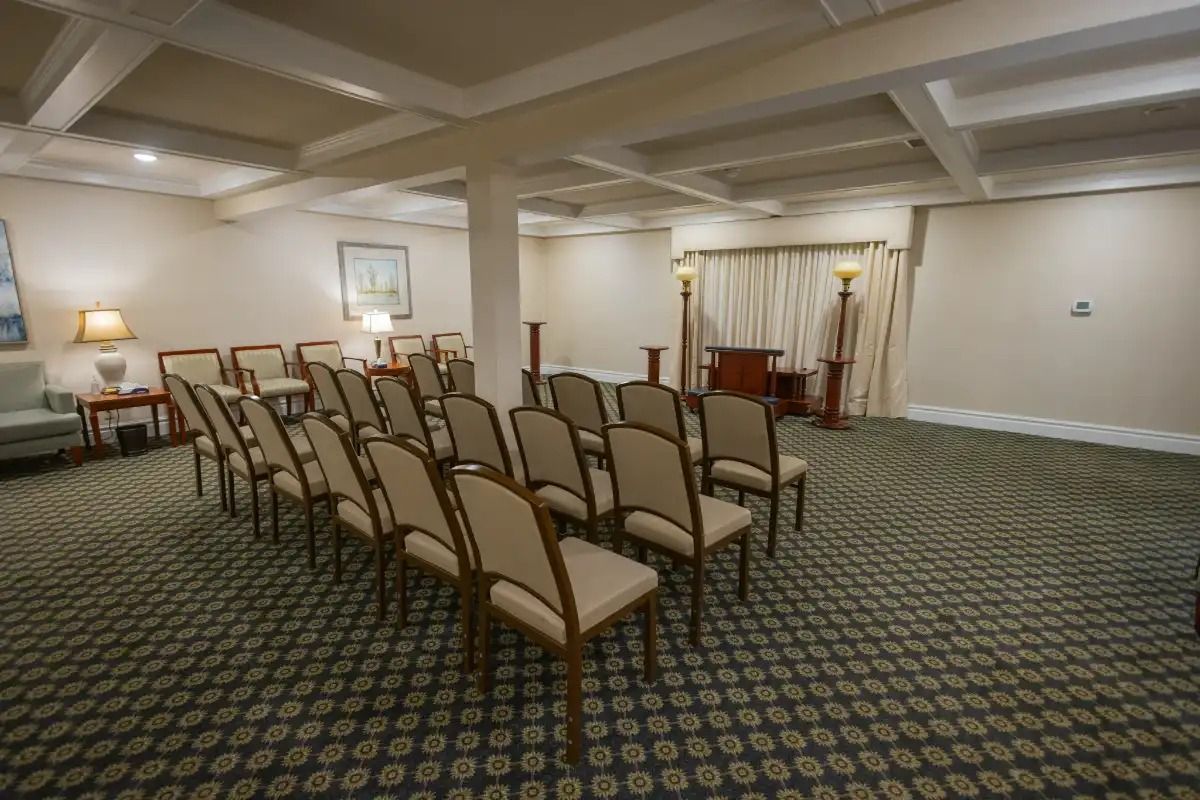 An empty chapel with rows of chairs, carpet flooring, and a podium. Beige and gold tones.