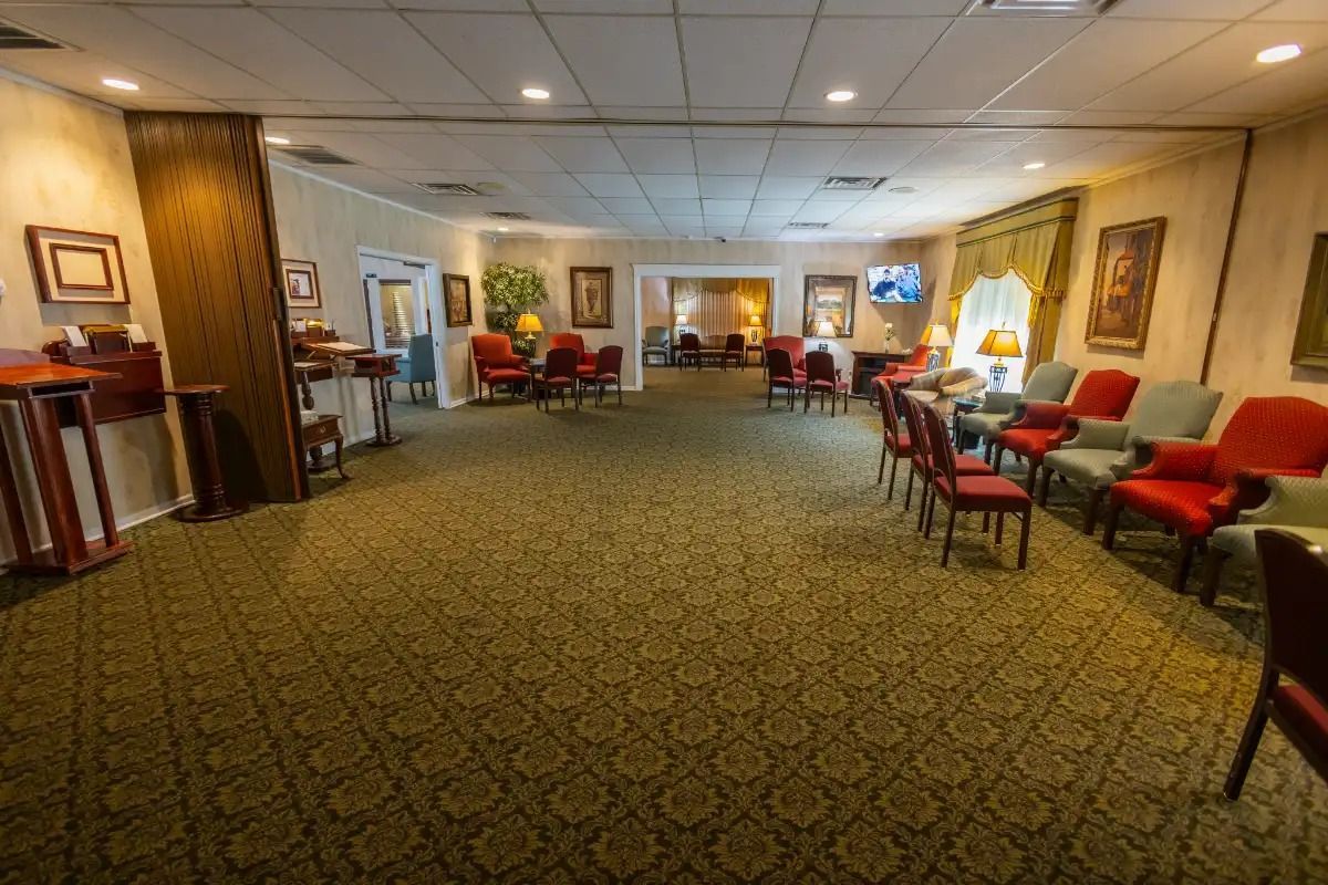 Interior of a funeral home, with seating, carpet, and art. Lighting is warm.