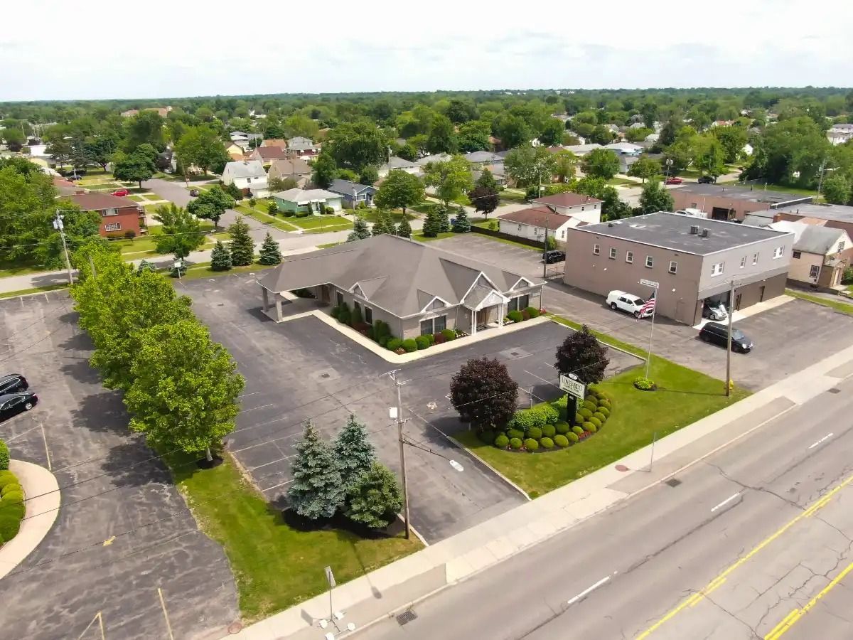 Aerial view of office buildings with parking, trees, and residential neighborhood in background.