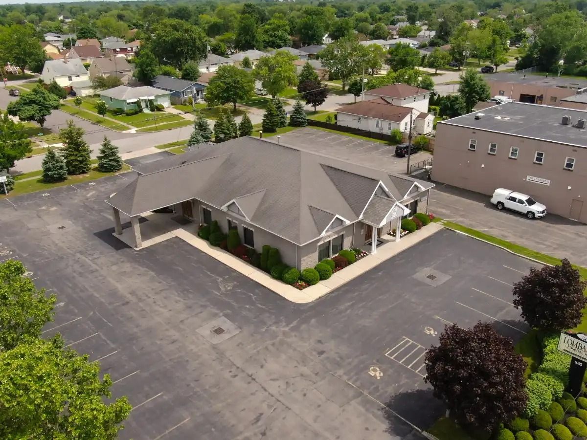 Aerial view of a gray building with a large parking lot in a suburban area with trees.