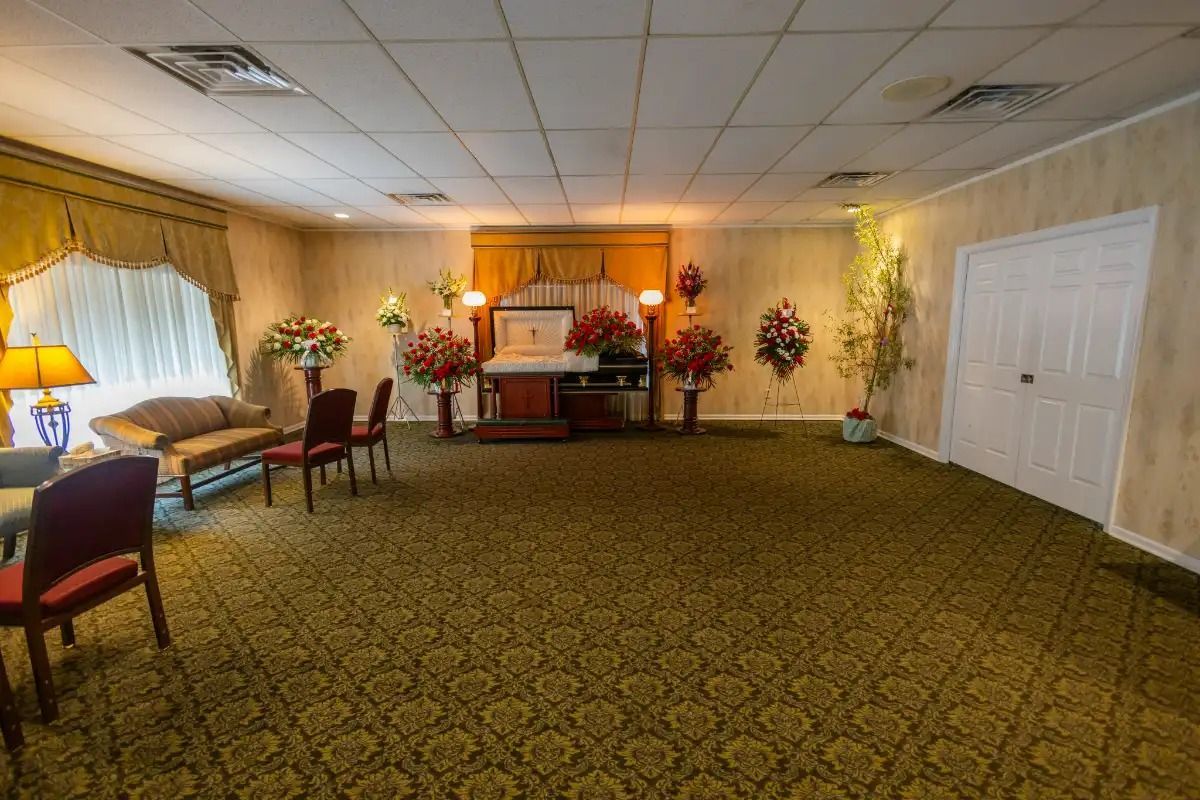Interior of a funeral home chapel with casket, floral arrangements, chairs, and seating.