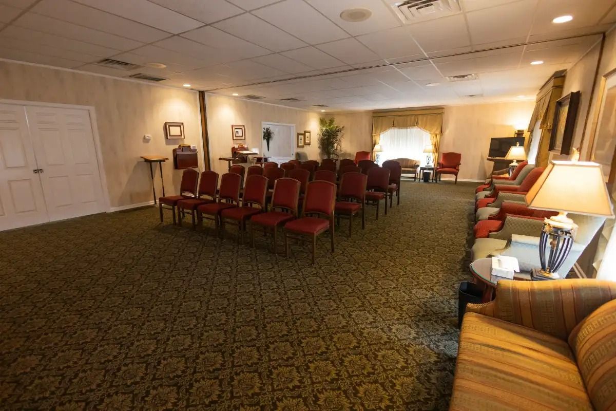 A funeral home chapel with rows of chairs, carpet, and a seated area.
