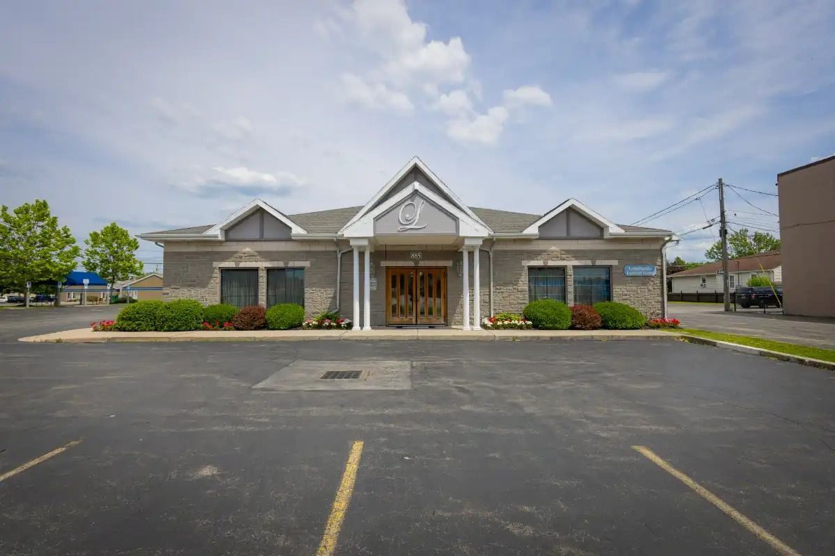 Building with stone facade, double doors, and parking lot under a cloudy sky.