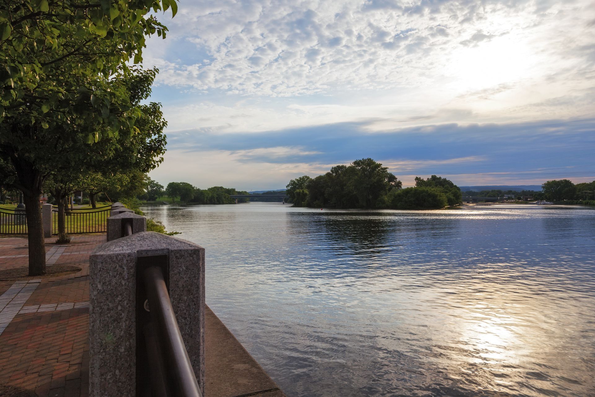 River scene with cloudy sky, trees lining the shore, and an island in the distance.