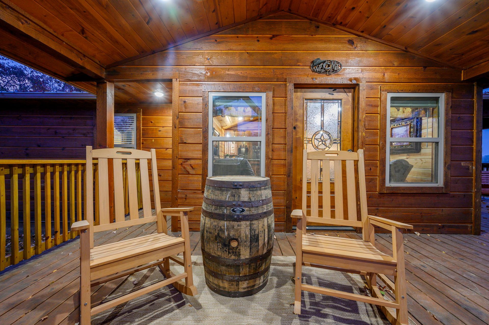 Two wooden rocking chairs on a cabin porch, facing a whiskey barrel table under a covered deck.
