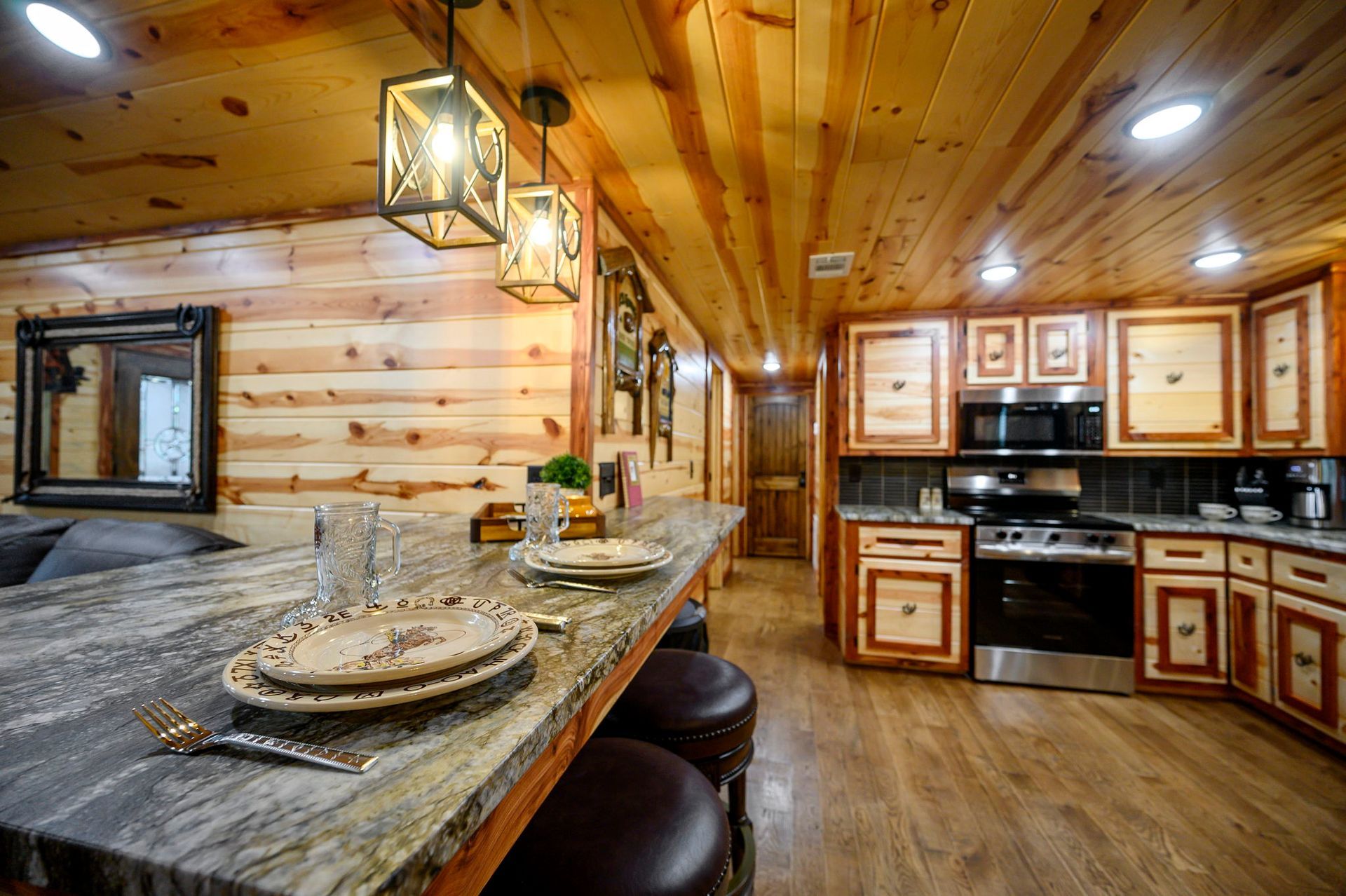 A rustic kitchen featuring wooden walls and ceiling, a long stone countertop with place settings, and stainless appliances.
