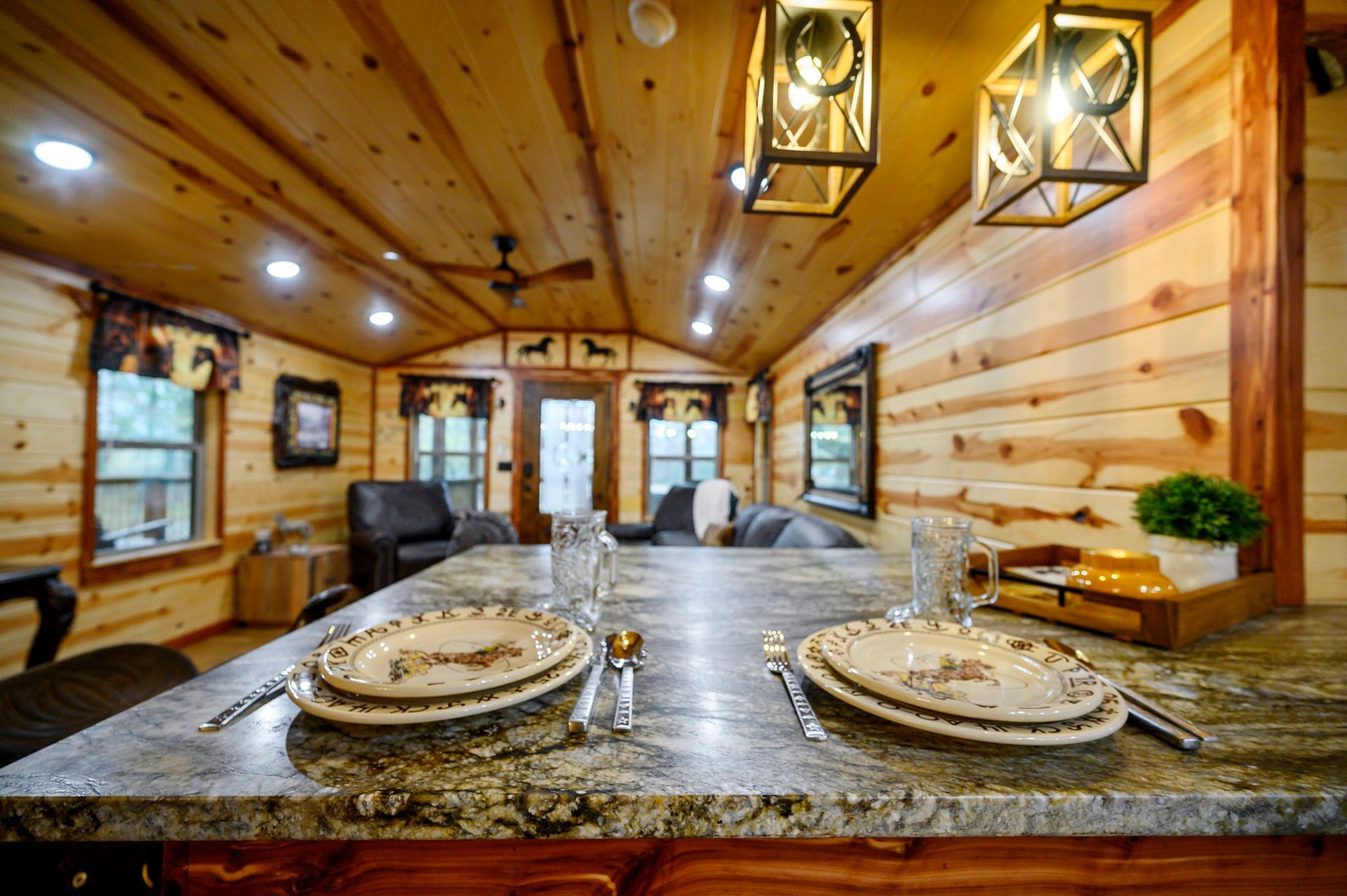 A stone kitchen island with two place settings in a wood-paneled cabin room with a living area in the background.