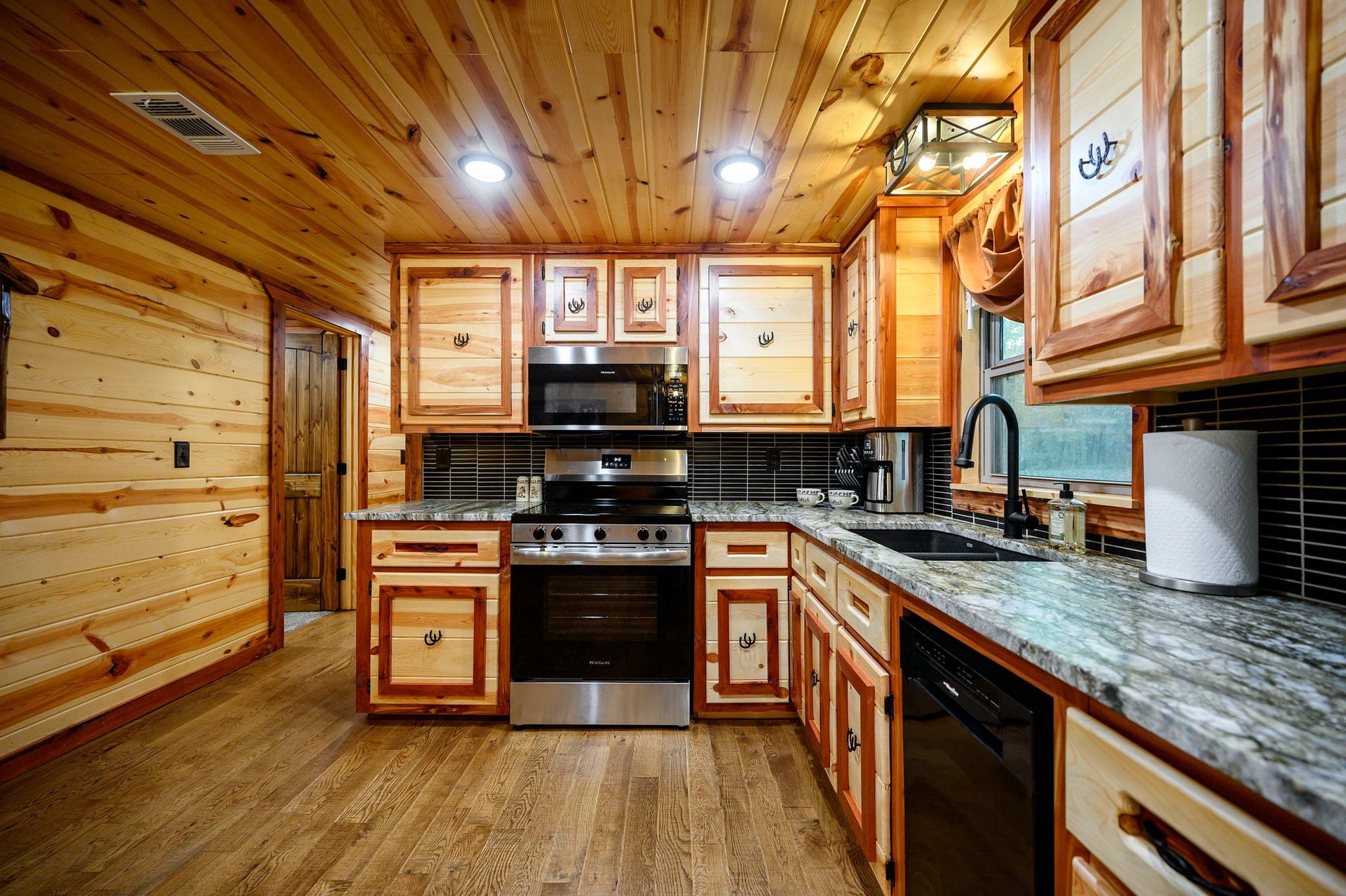 A rustic kitchen featuring wooden walls and cabinets, a stainless steel oven, and granite countertops.