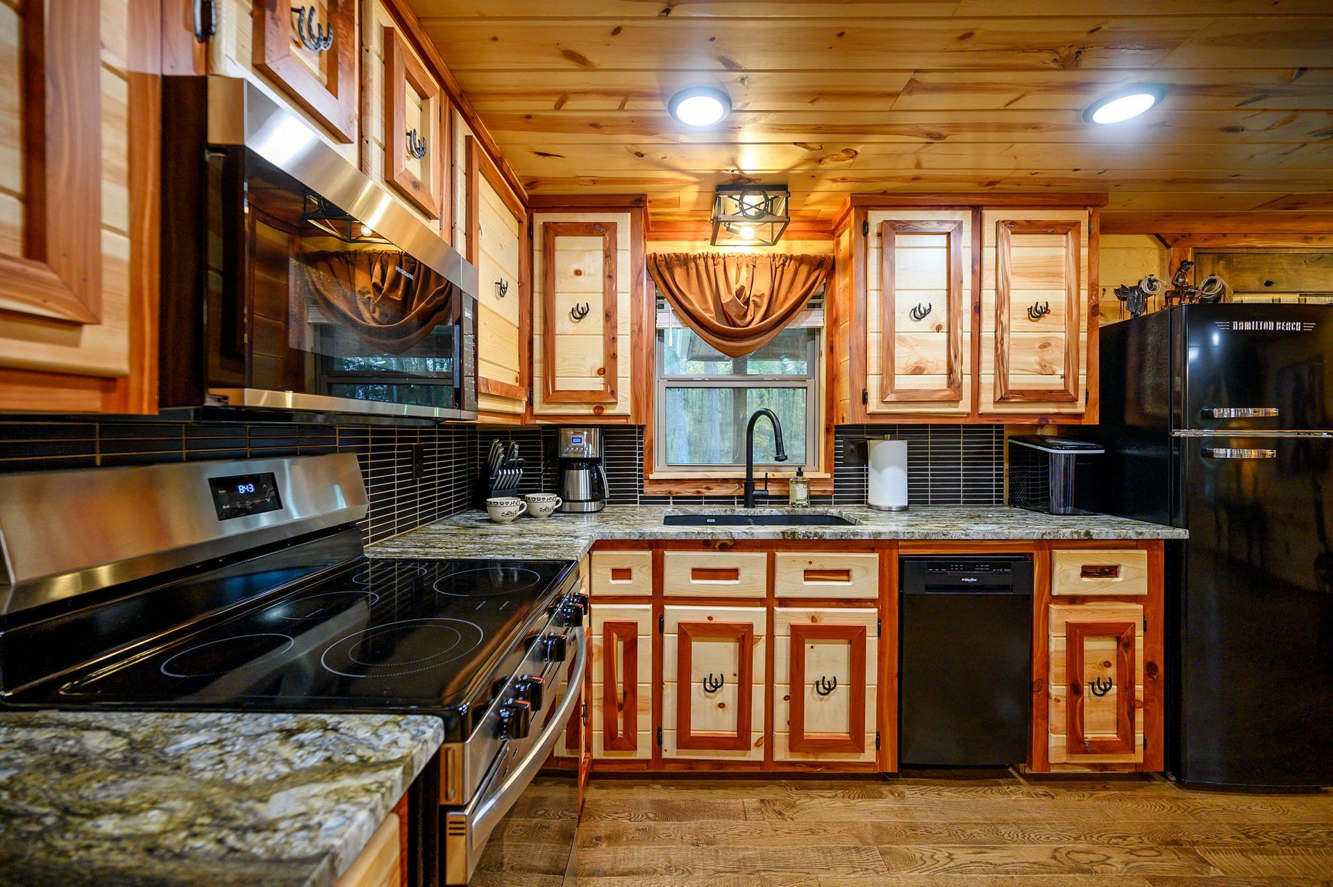 Rustic cabin kitchen with wood cabinets, black appliances, and granite countertops.