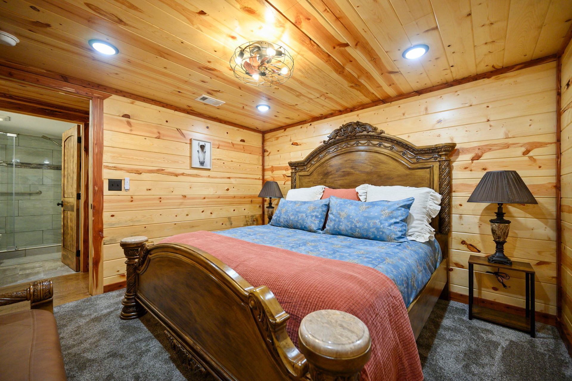 A cozy bedroom with wood-paneled walls and ceiling, featuring a large wooden bed with blue bedding and a coral throw.