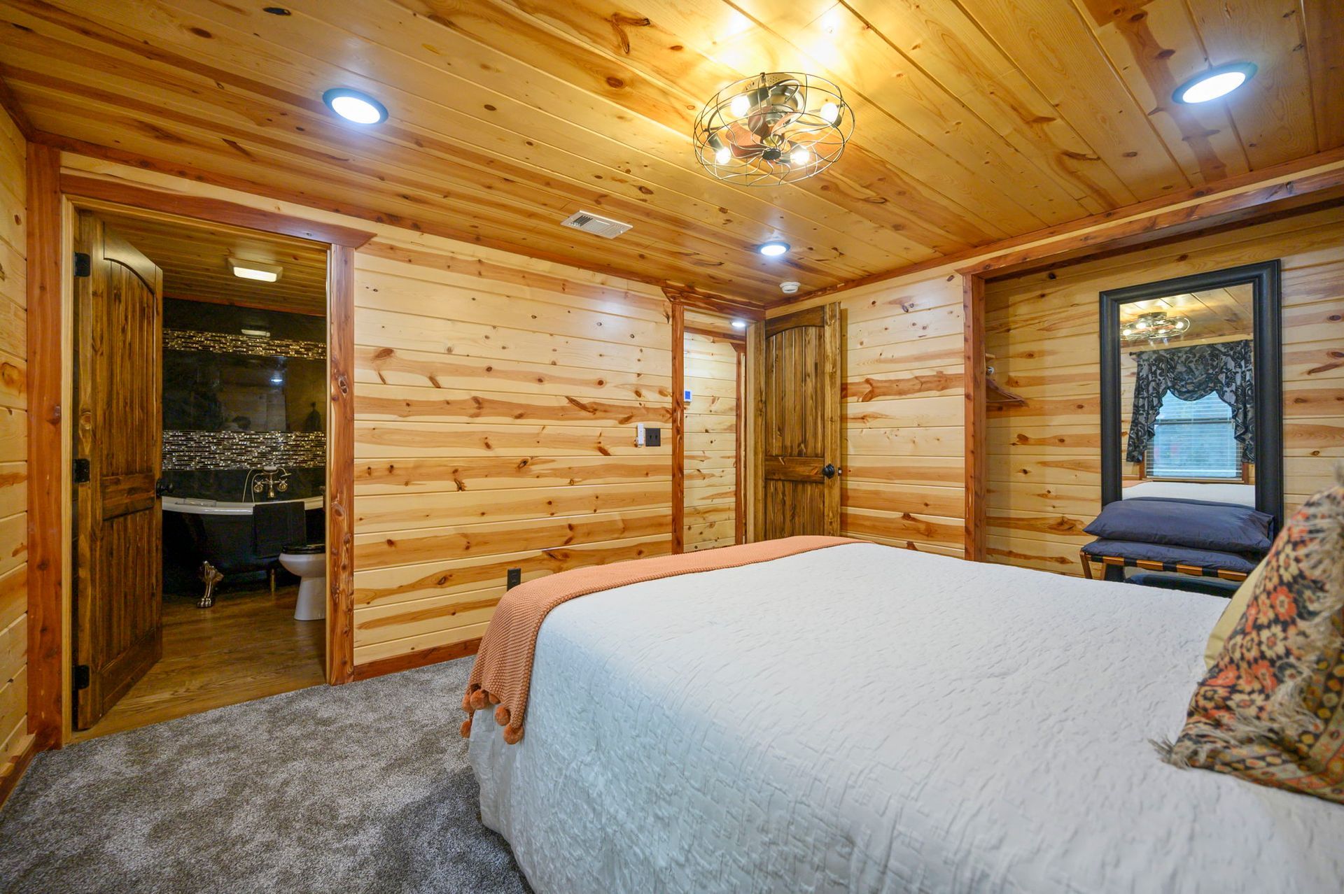 A bedroom with wood-paneled walls, a large bed with white bedding, and an open doorway revealing a bathroom.