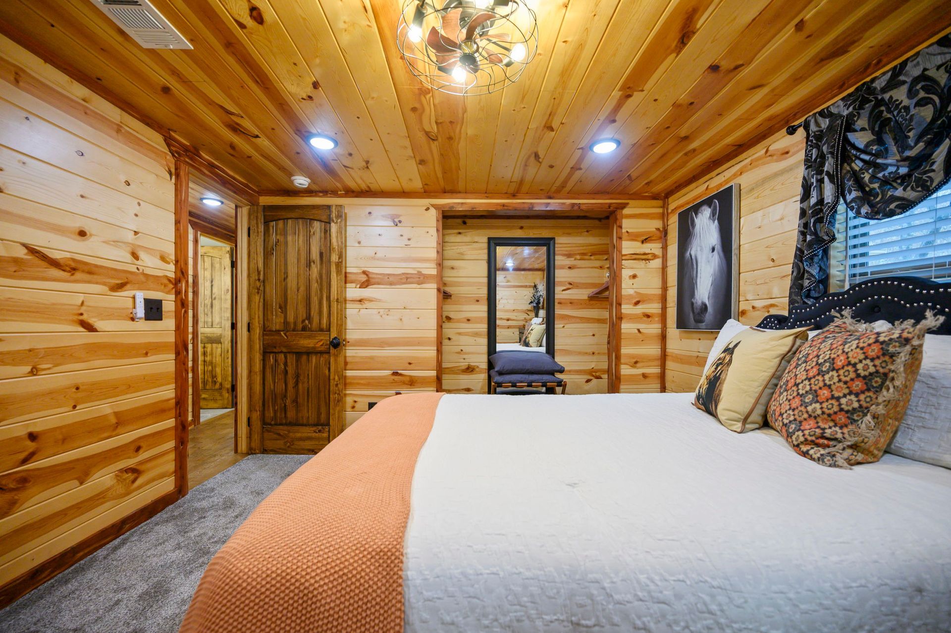 A rustic bedroom with wood-paneled walls, a white bed with patterned pillows, and a doorway leading to a walk-in closet.