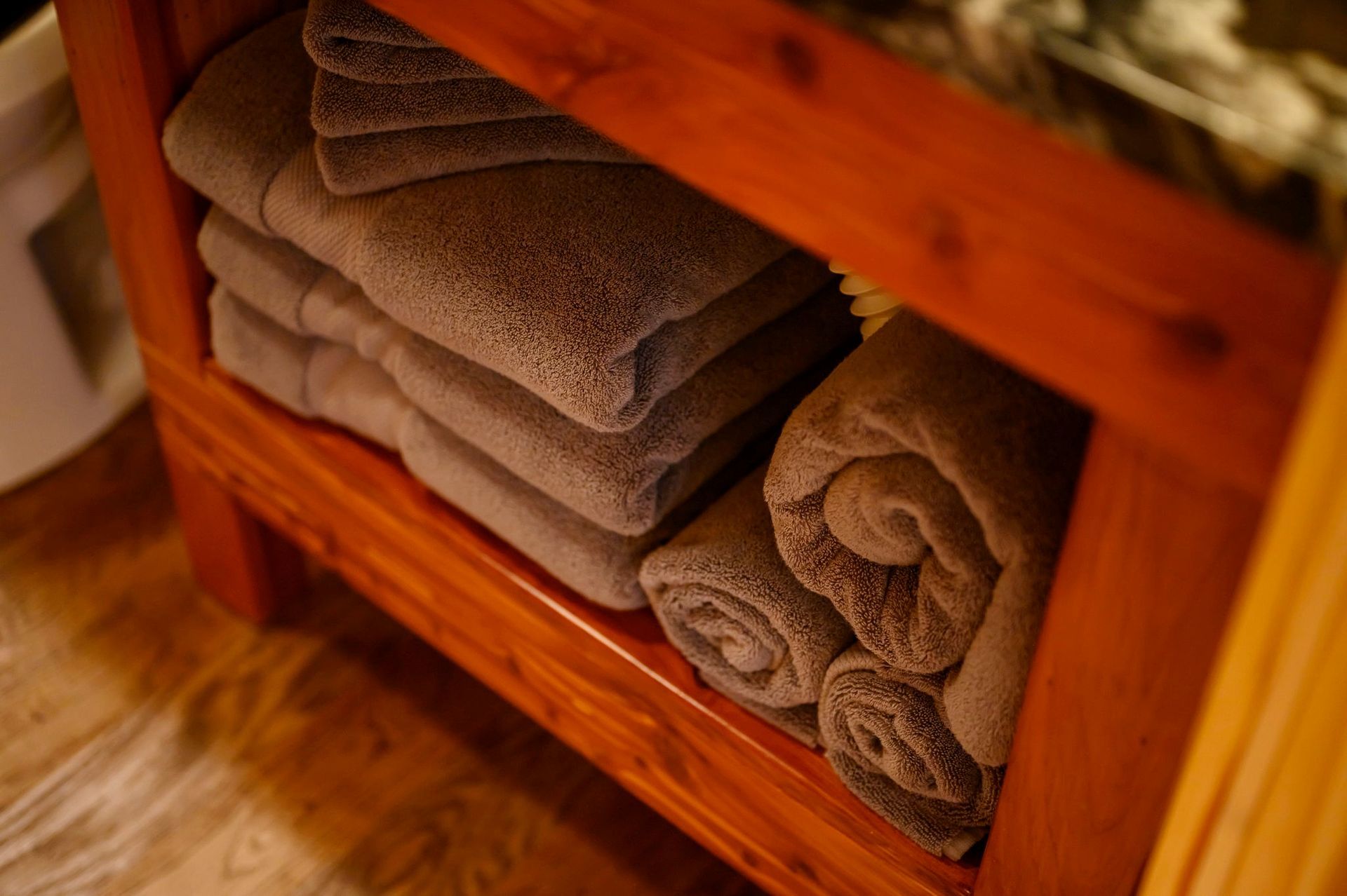 Stacked and rolled neutral-colored towels neatly arranged on the lower shelf of a wooden bathroom vanity.