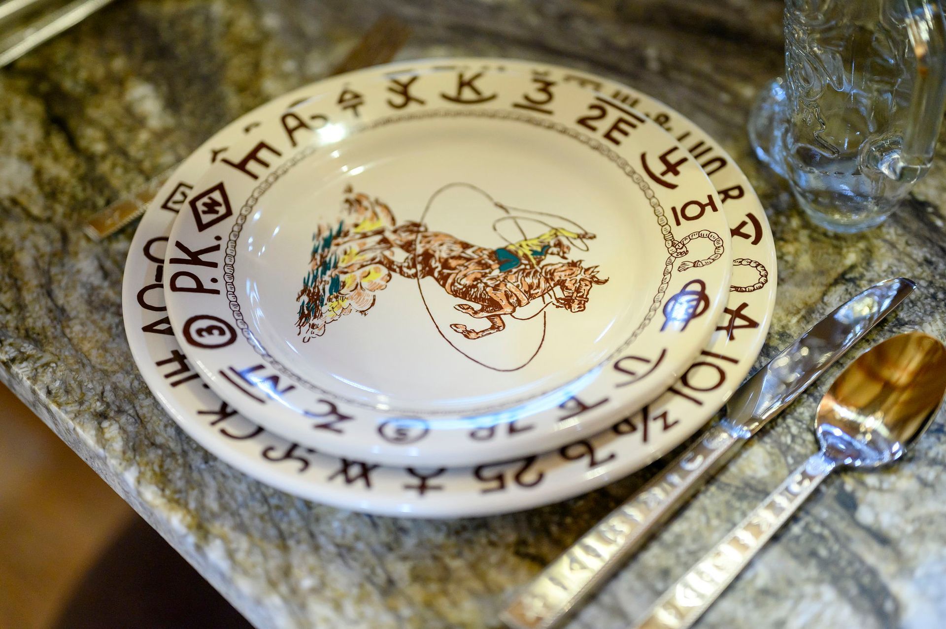 Two stacked decorative plates featuring western cattle brands on the rims and a cowboy on the top plate, set on a counter.