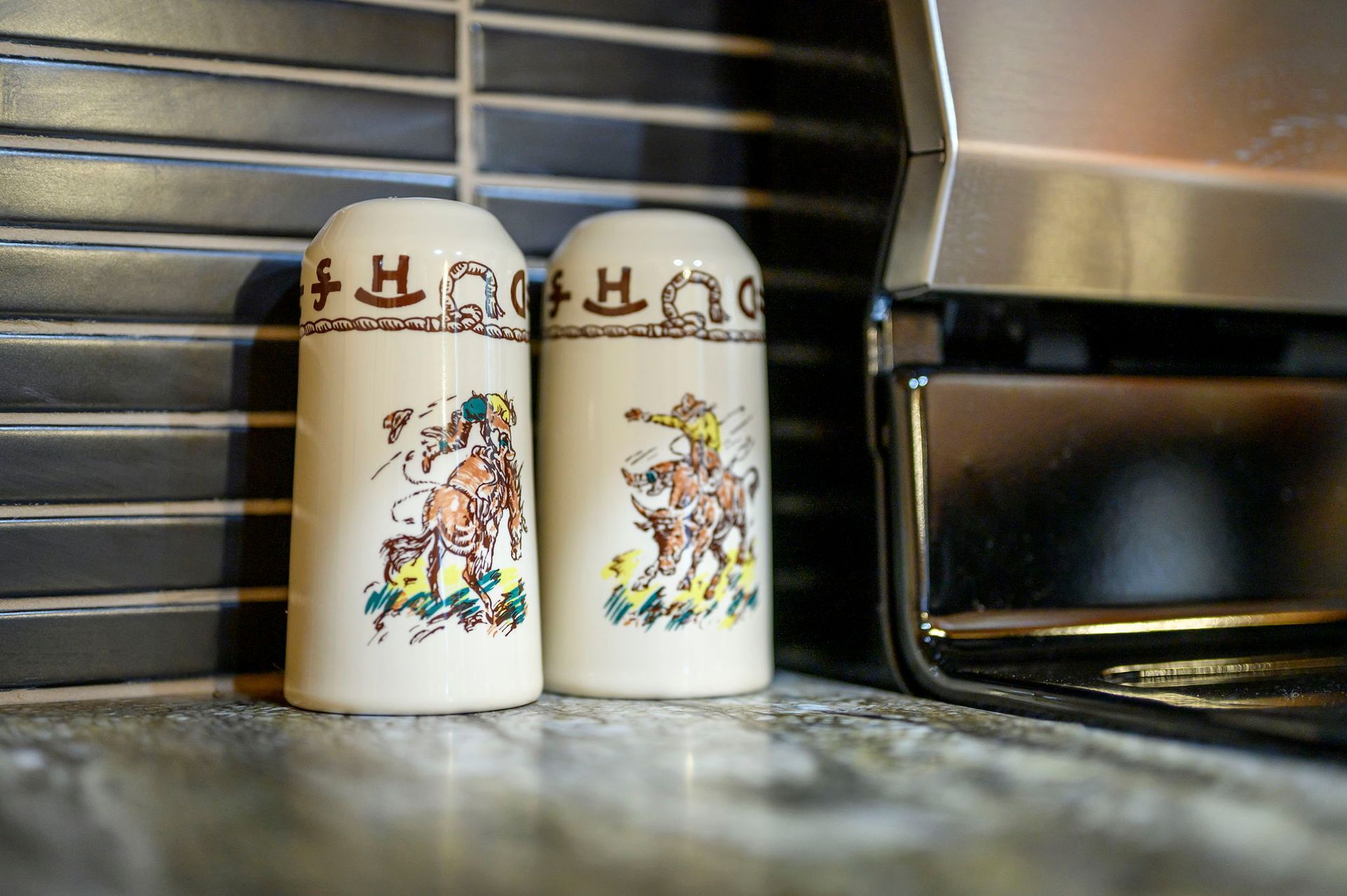 Two vintage-style ceramic salt and pepper shakers with Western rodeo illustrations, sitting on a kitchen countertop.
