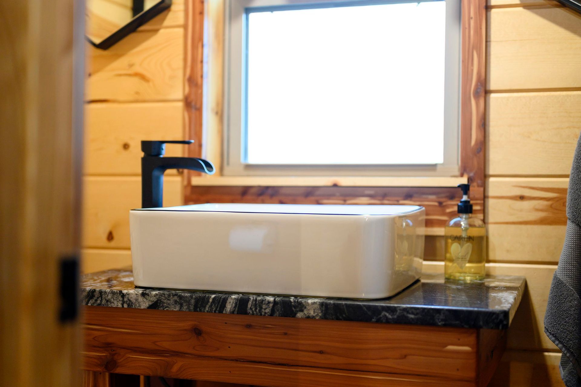 A white rectangular vessel sink with a black faucet on a stone vanity in a bathroom with wooden walls.