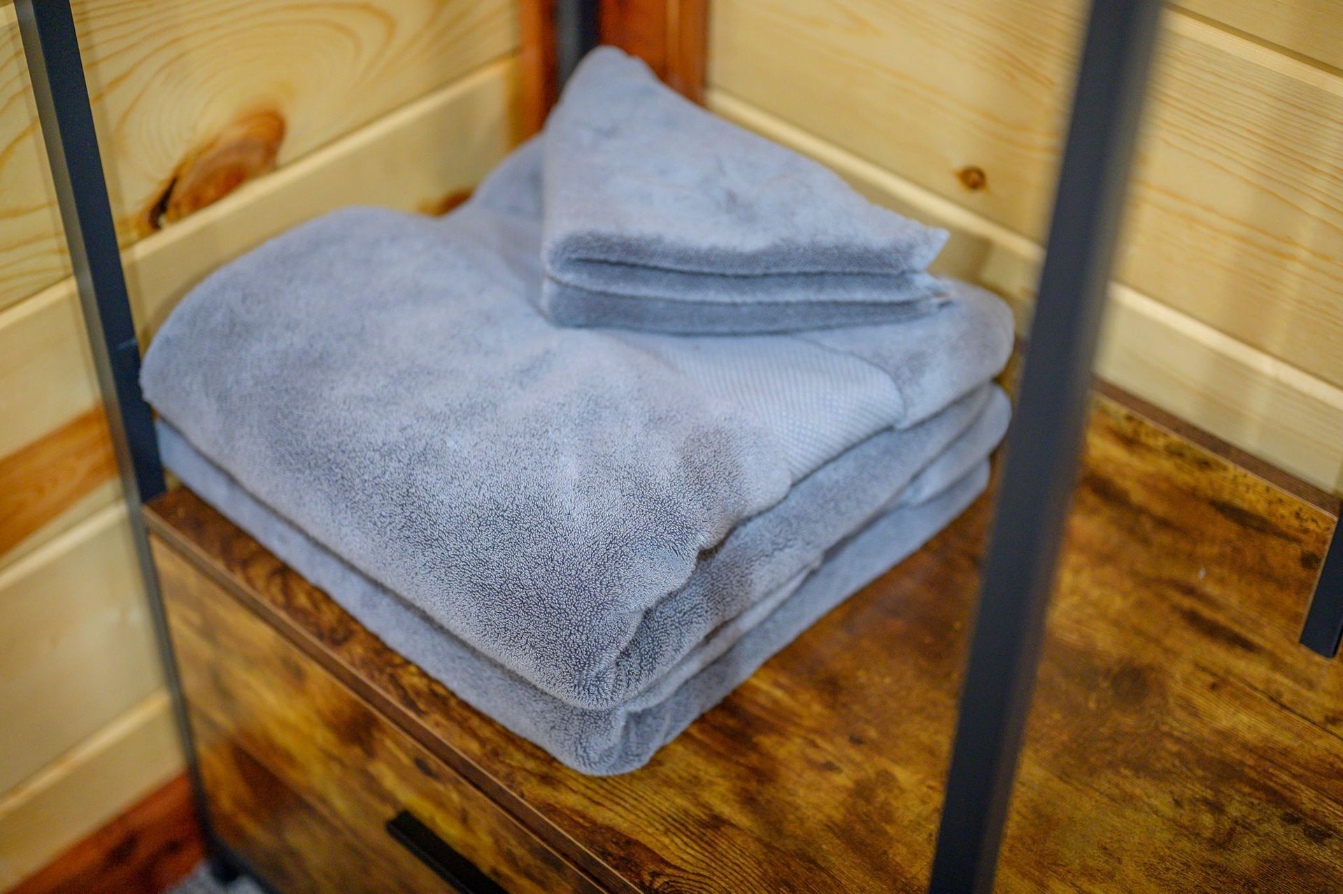 A stack of folded blue towels sits on a wooden shelf against a light wood-paneled wall.