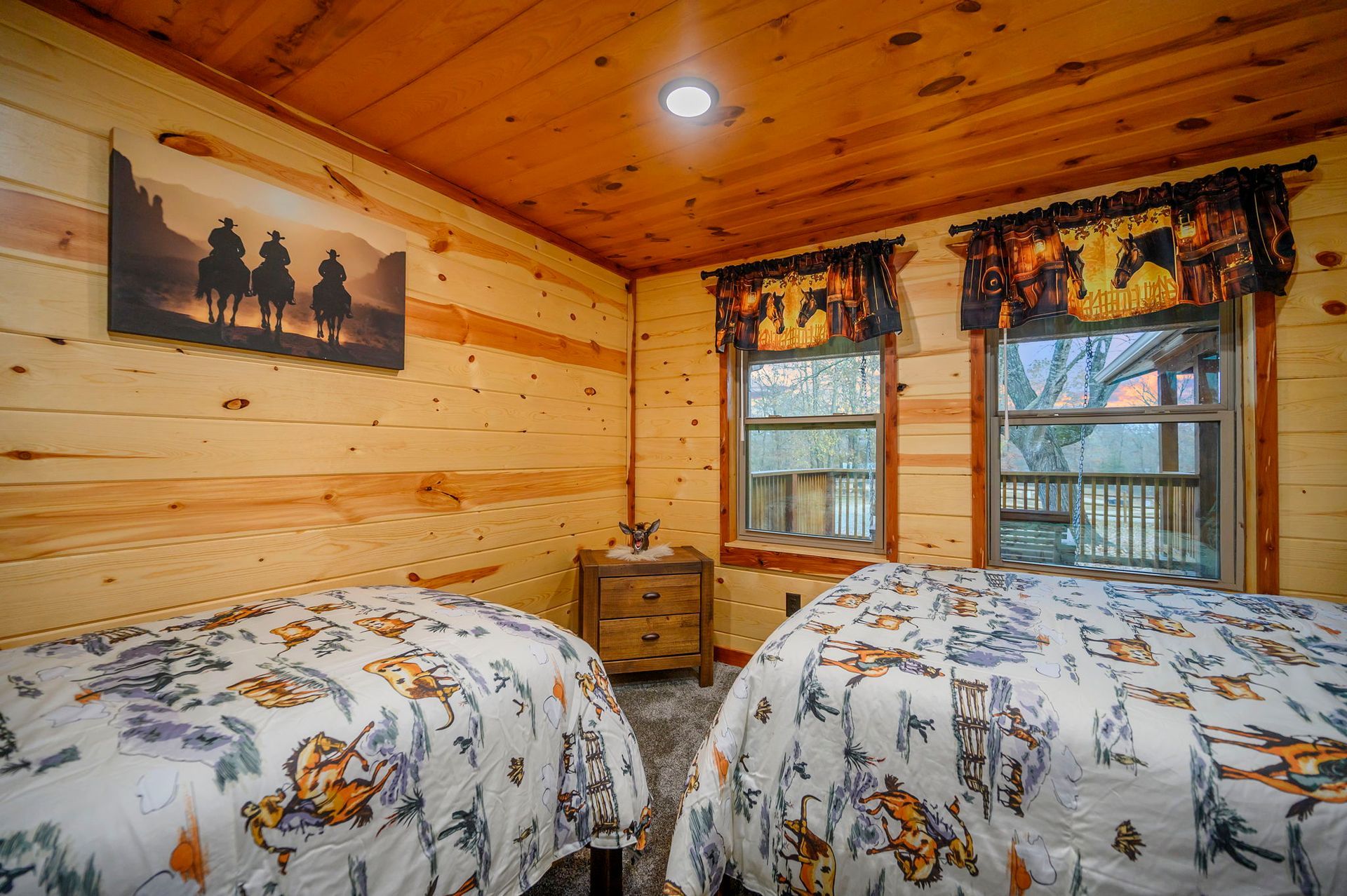 A rustic bedroom featuring wood-paneled walls, two twin beds with horse-patterned quilts, and a small wooden nightstand.
