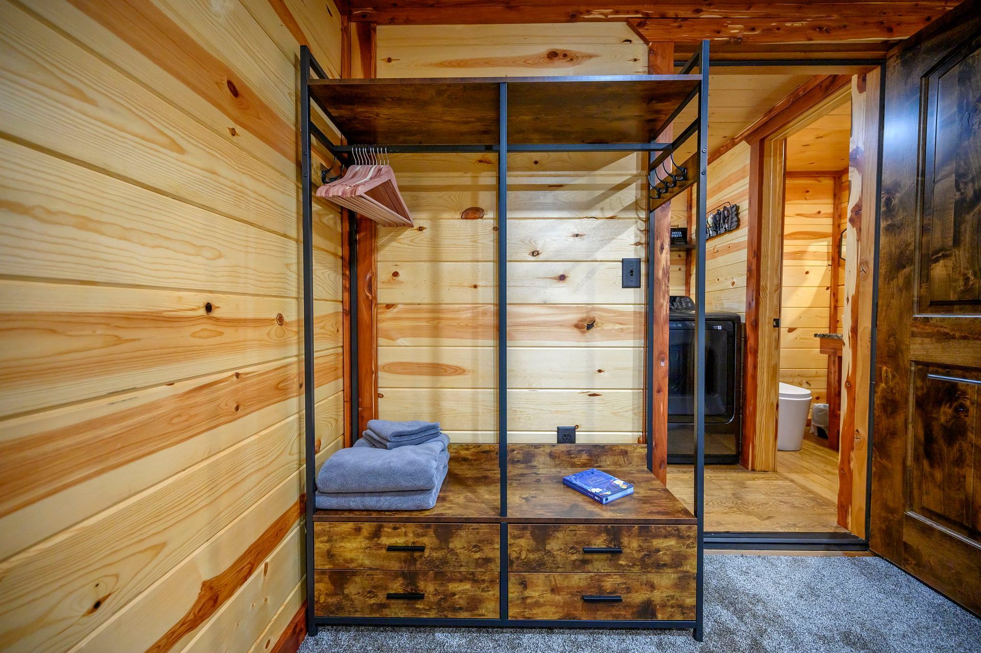A rustic metal and wood shelving unit with hangers, folded towels, and drawers against a wood-paneled wall.