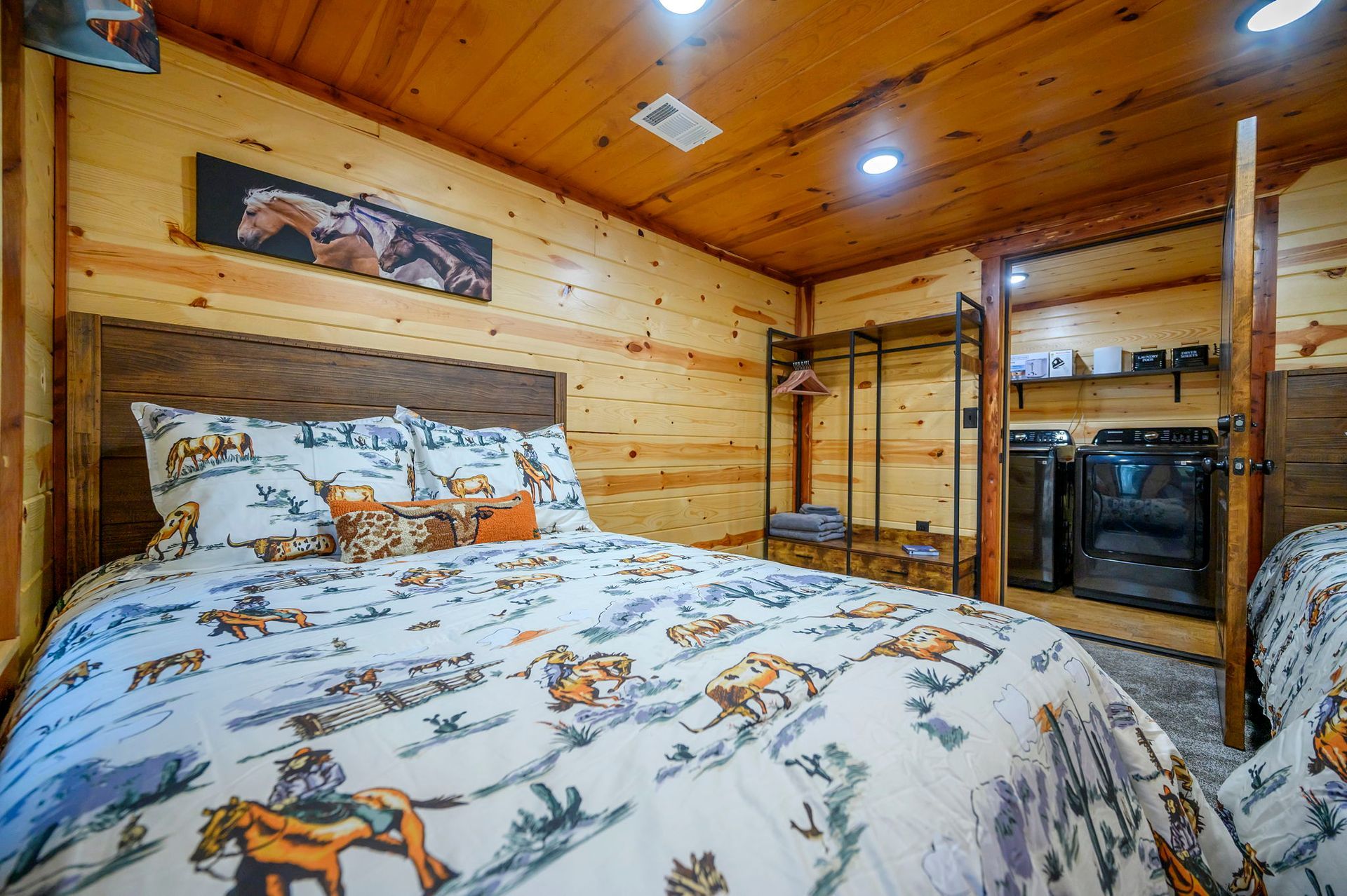A rustic bedroom with wood-paneled walls, featuring a bed with horse-patterned bedding and an open closet area.