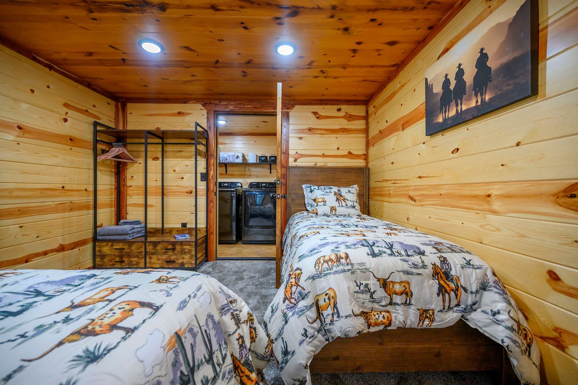 A rustic bedroom with two twin beds, wood-paneled walls, a metal wardrobe, and a small laundry room in the background.