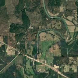 An aerial view showing a winding river flowing through forested areas and agricultural fields, crossed by a long highway.