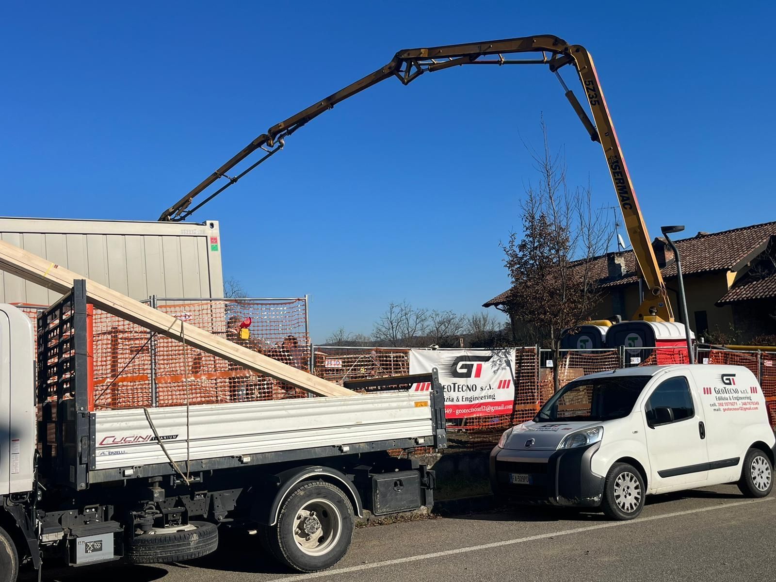 Cantiere con un'autopompa per calcestruzzo che si estende sopra un camion e un furgone bianco Geotecno Genova.