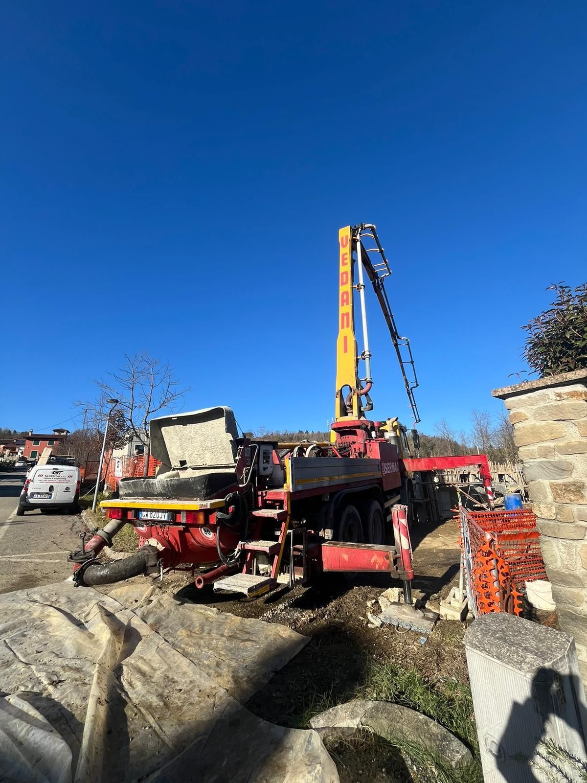 Un'autopompa per calcestruzzo contro un cielo azzurro, in un cantiere. I colori rosso e giallo sono ben visibili, con un braccio sollevato che si estende cantiere Geotecno Genova