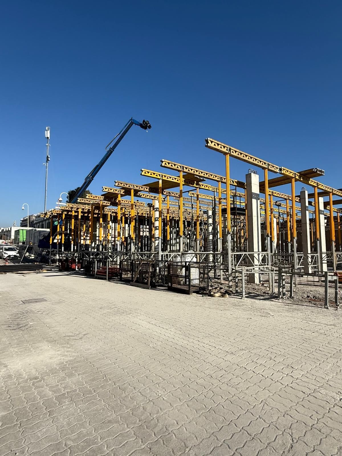 Cantiere con impalcature gialle e una gru contro un cielo azzurro terso. Pilastri di cemento parzialmente costruiti Geotecno Genova