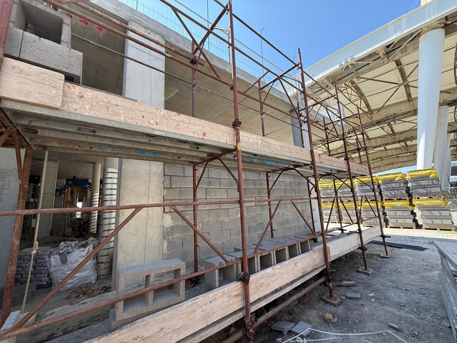 Cantiere edile con impalcature addossate a un edificio, caratterizzato da blocchi di cemento, cemento e materiali da costruzione.