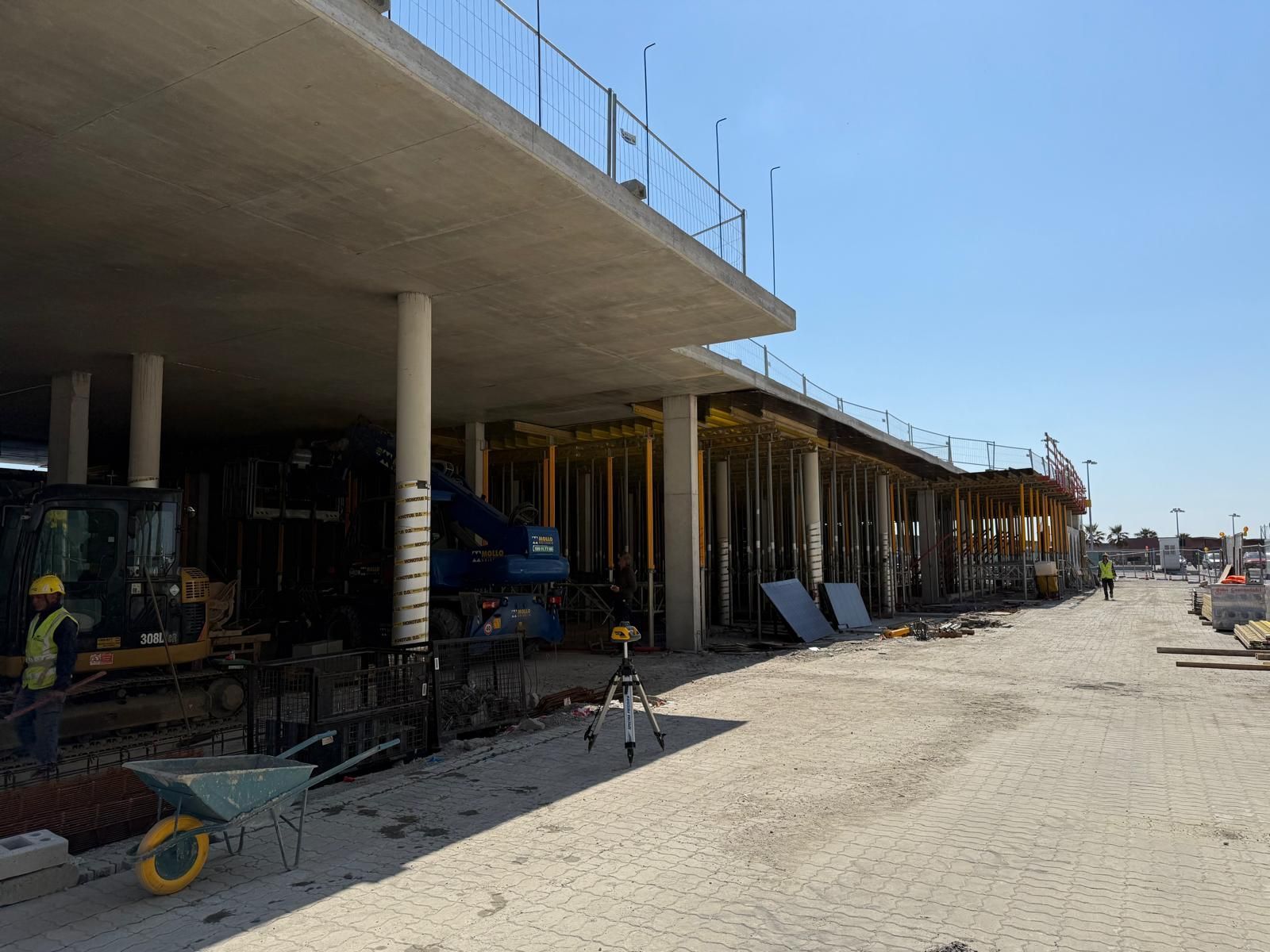 Cantiere con strutture in cemento sotto un cielo azzurro brillante. Sono presenti carriole gialle e macchinari pesanti Geotecno Genova