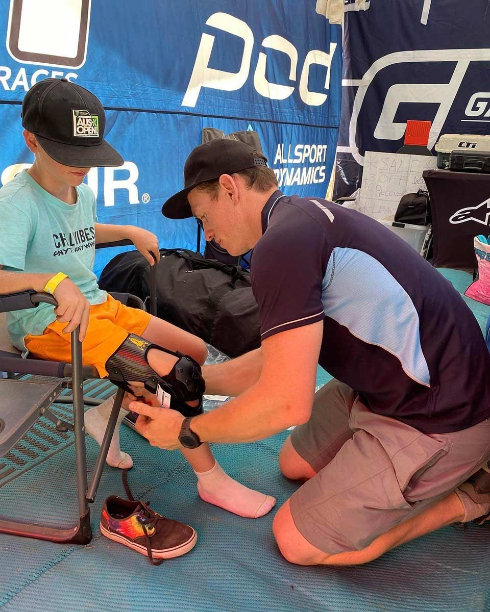 A Man is Kneeling Down Helping a Child Put on a Pair of Knee Brace — Gall Bros Medical in Robina, QLD