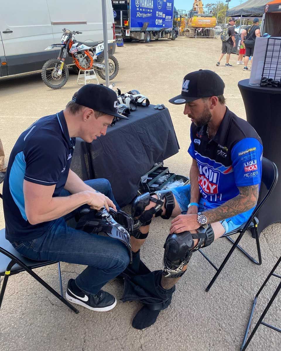 Two Men Are Sitting in Chairs in a Parking Lot Talking to Each Other — Gall Bros Medical in Robina, QLD