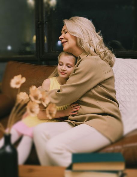 A woman is sitting on a couch hugging a little girl.