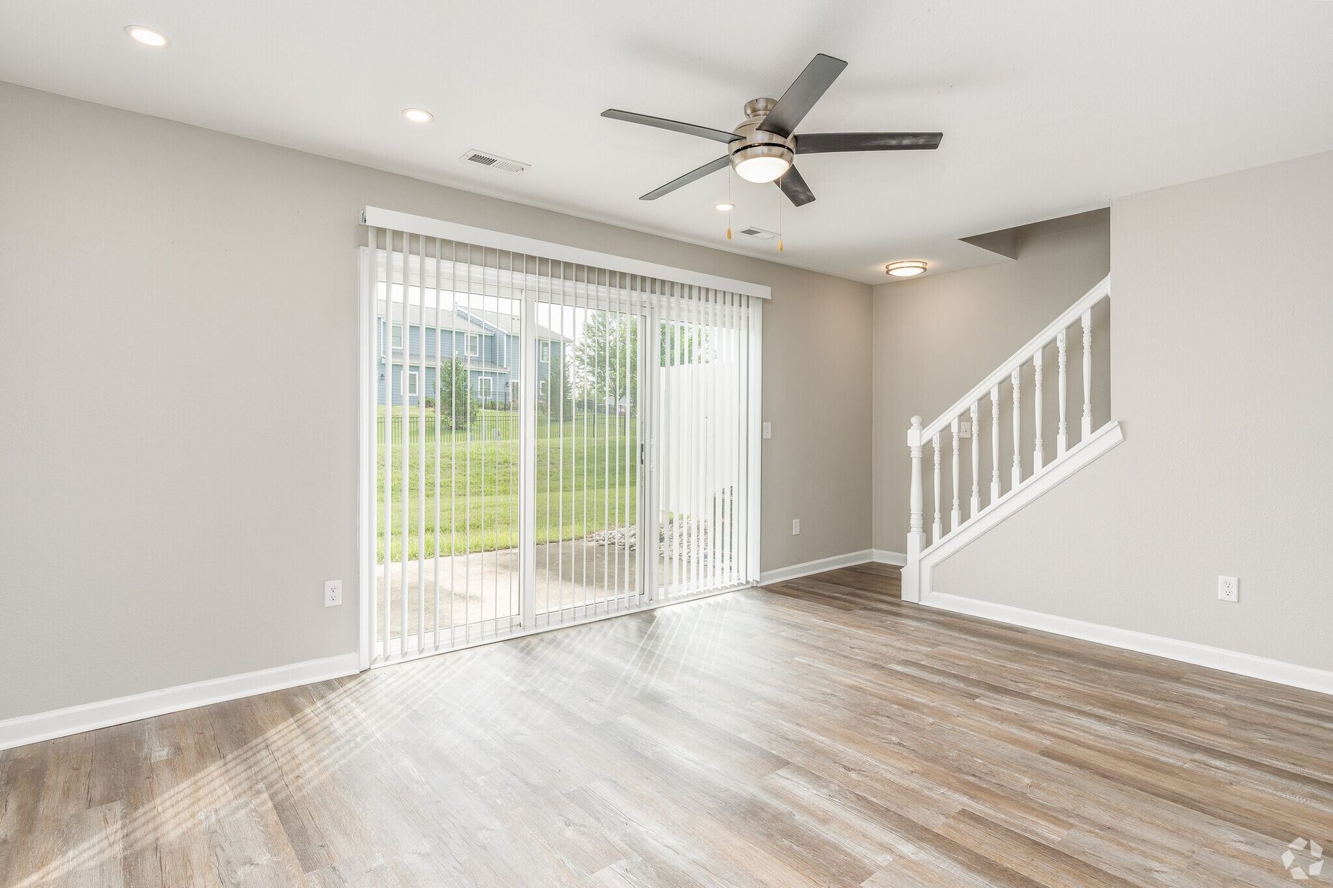 Living room with gray walls, wood floors, sliding glass door, stairs, and ceiling fan.