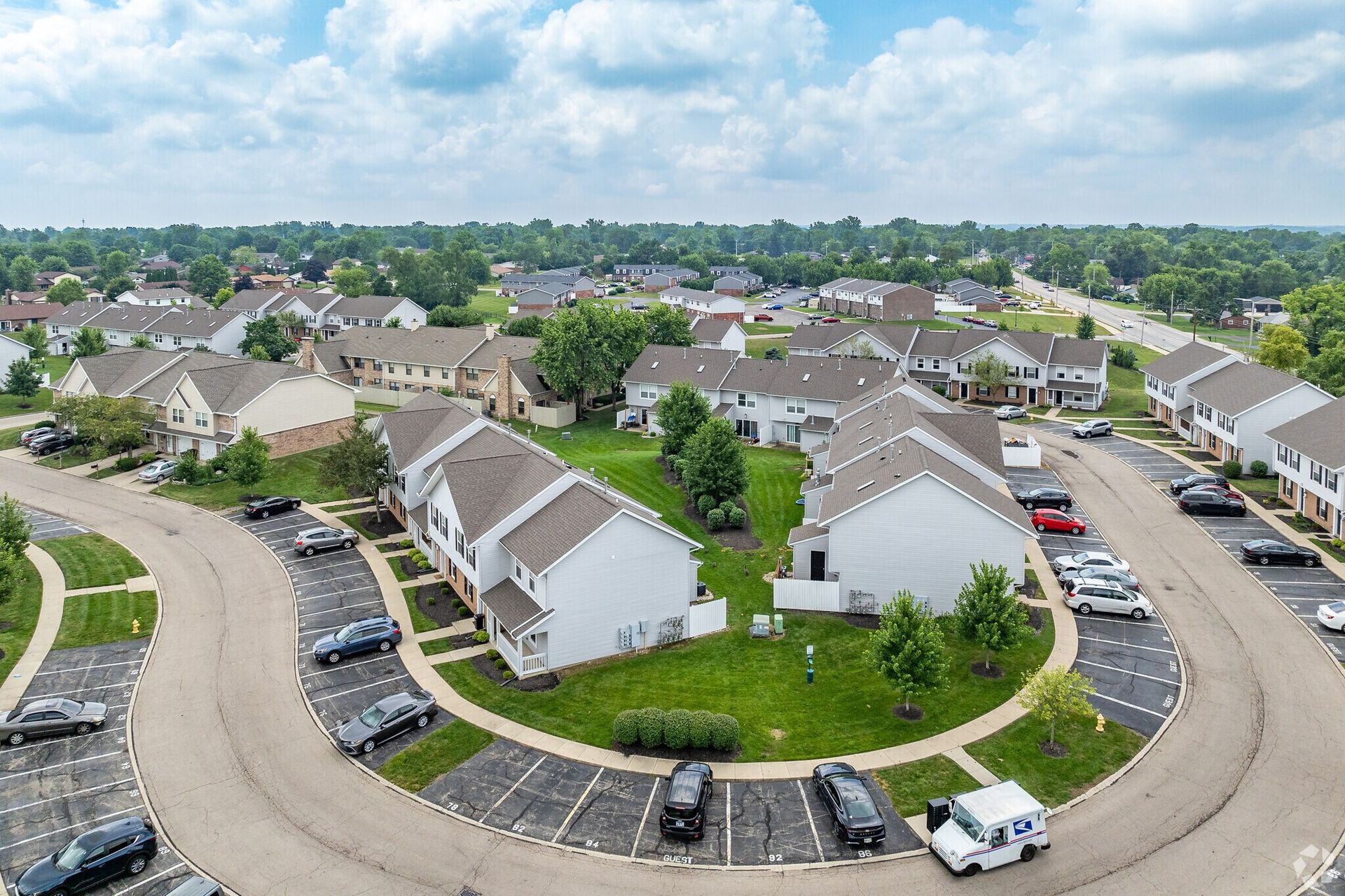 Aerial view of a suburban neighborhood with townhouses and parked cars on a sunny day.