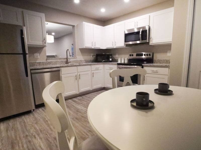 Modern white kitchen with stainless steel appliances and a round dining table.