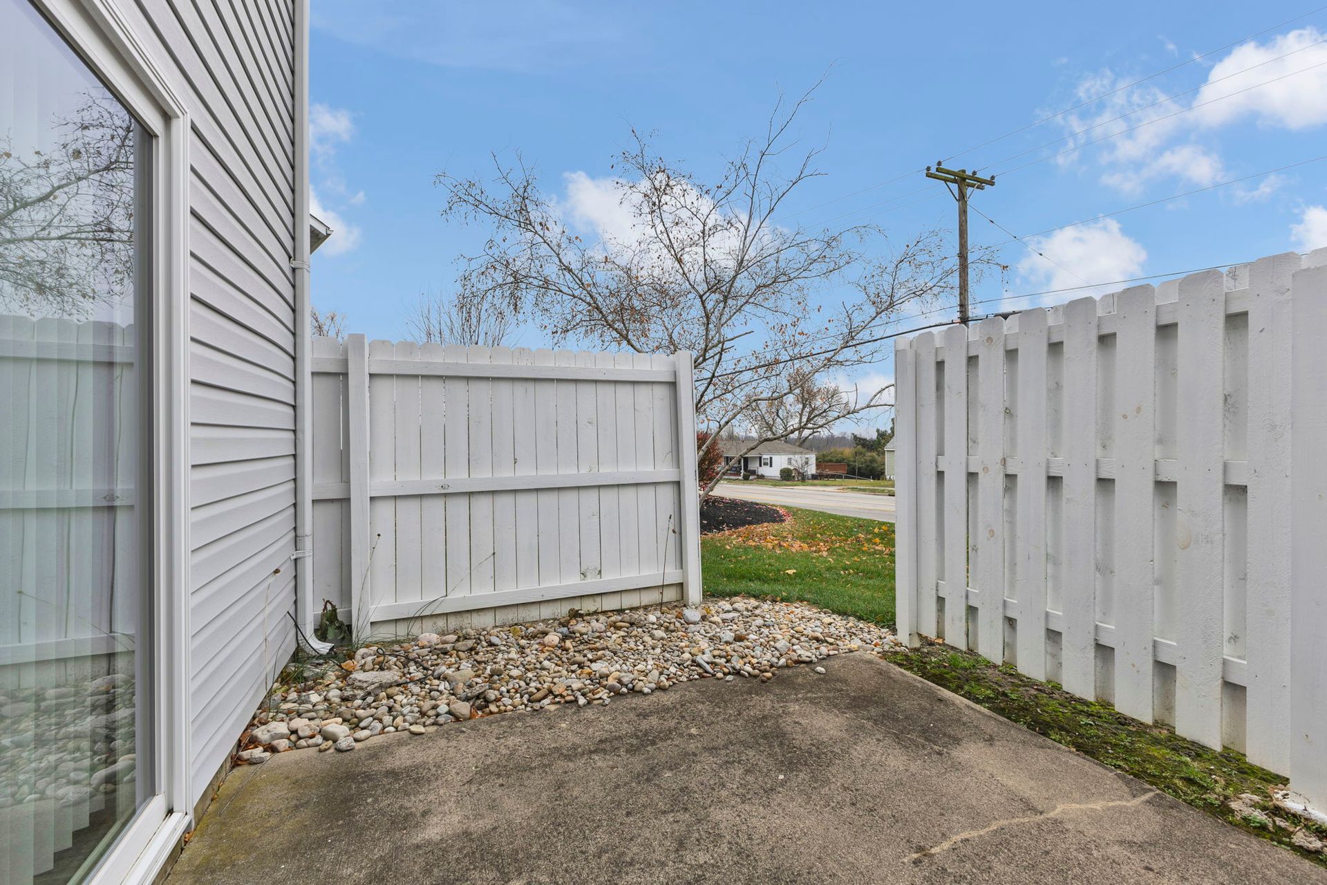 Small fenced patio with concrete slab, rocks, and a sliding glass door.