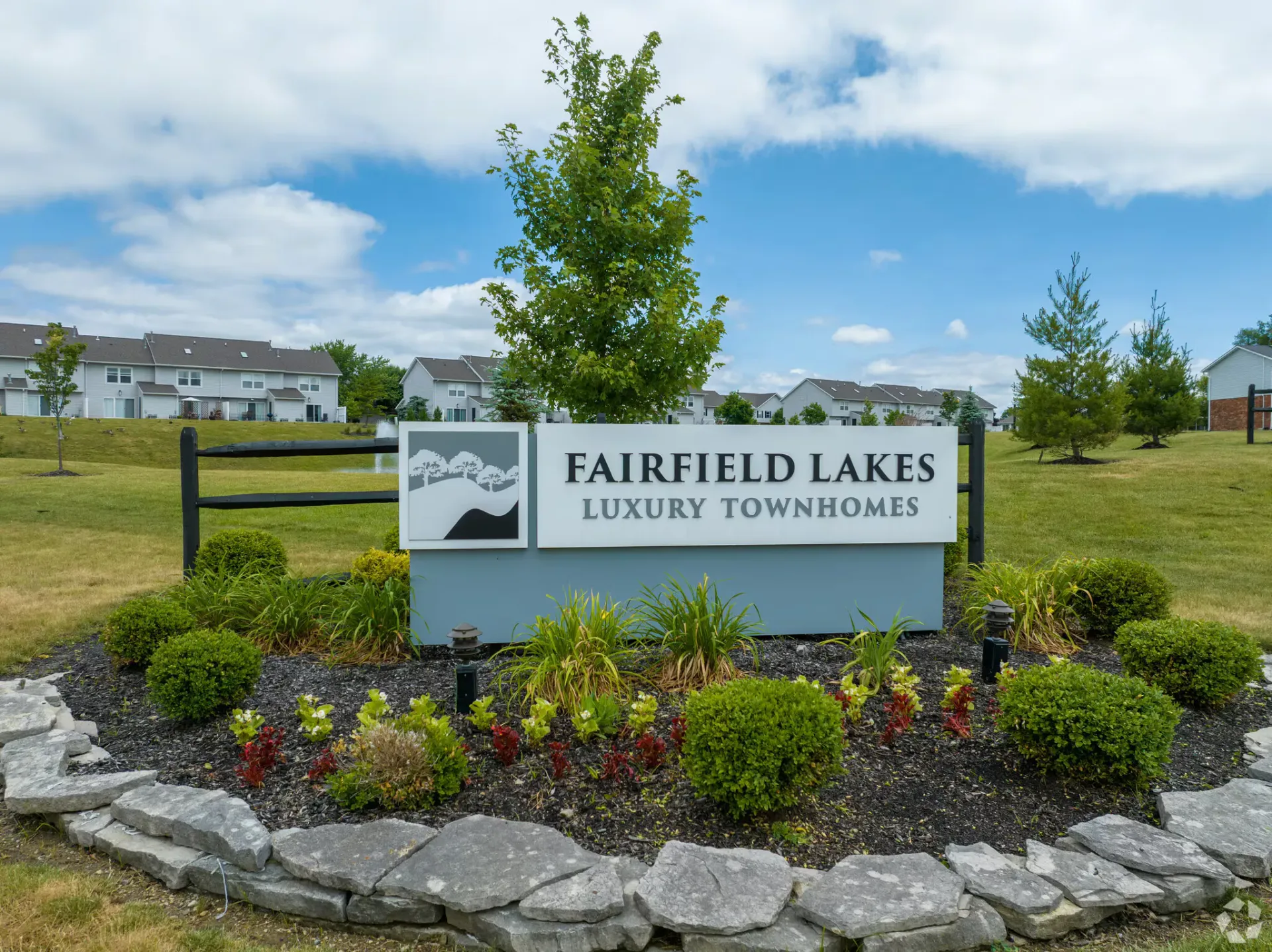 Sign for Fairfield Lakes Luxury Townhomes with landscaping and townhouses in the background.