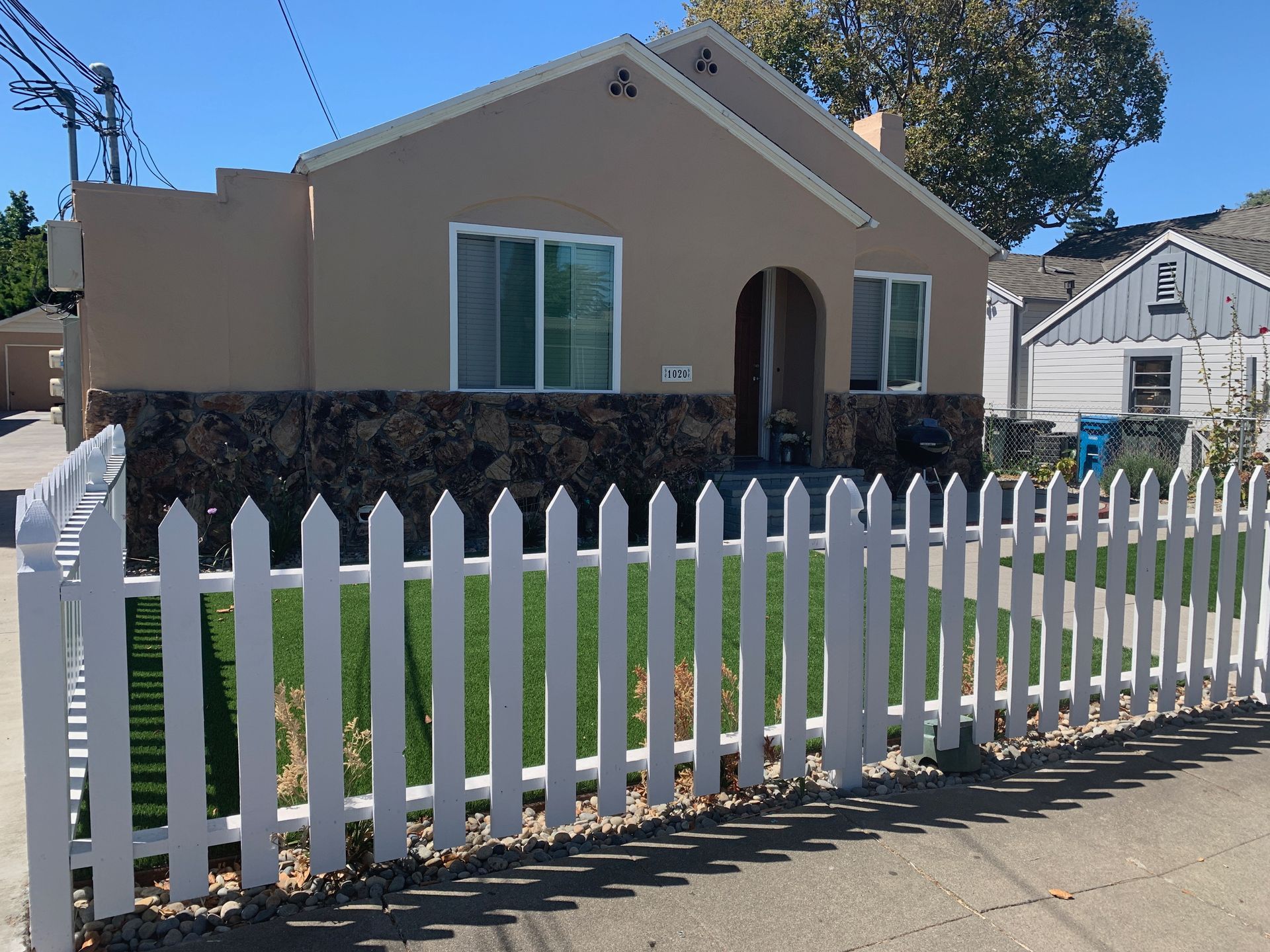 Tan house with white picket fence and green lawn.