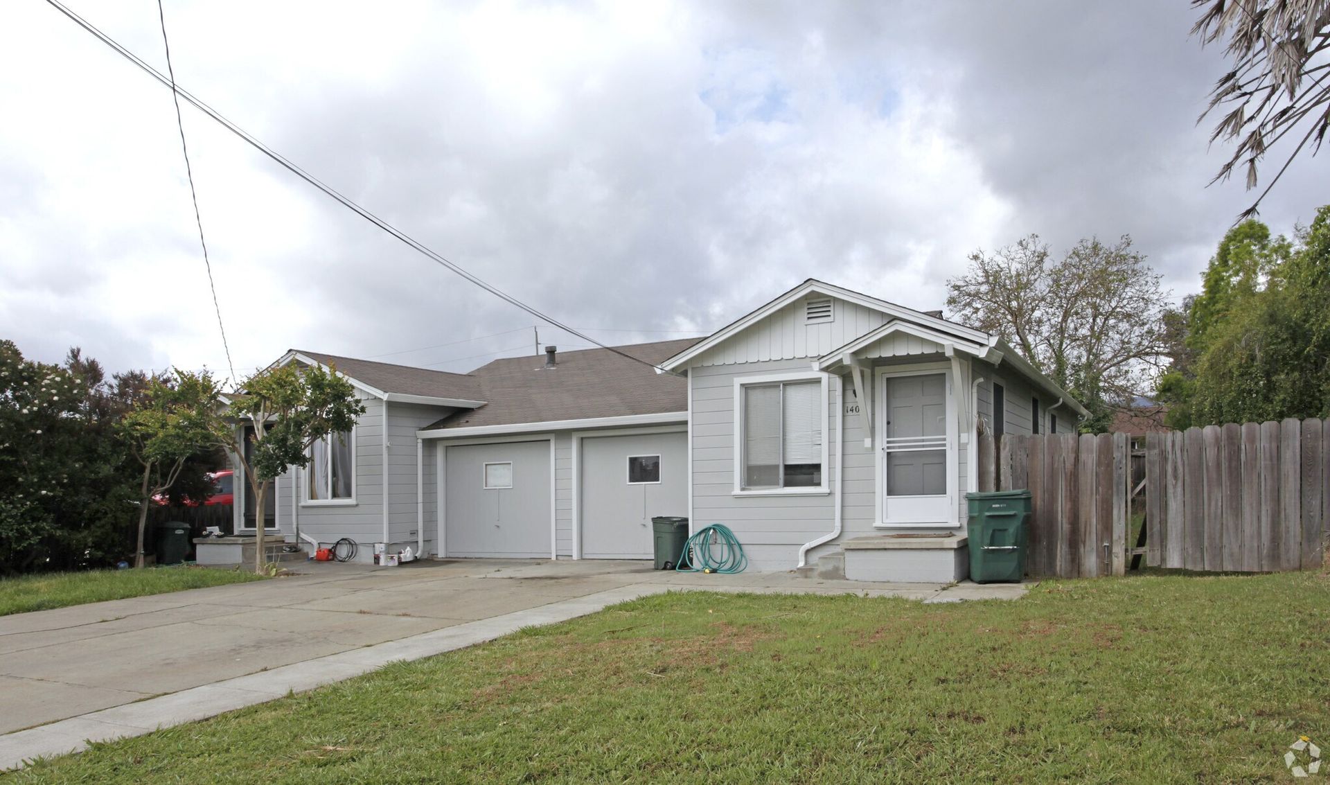 Gray house with a driveway and green lawn under a cloudy sky.