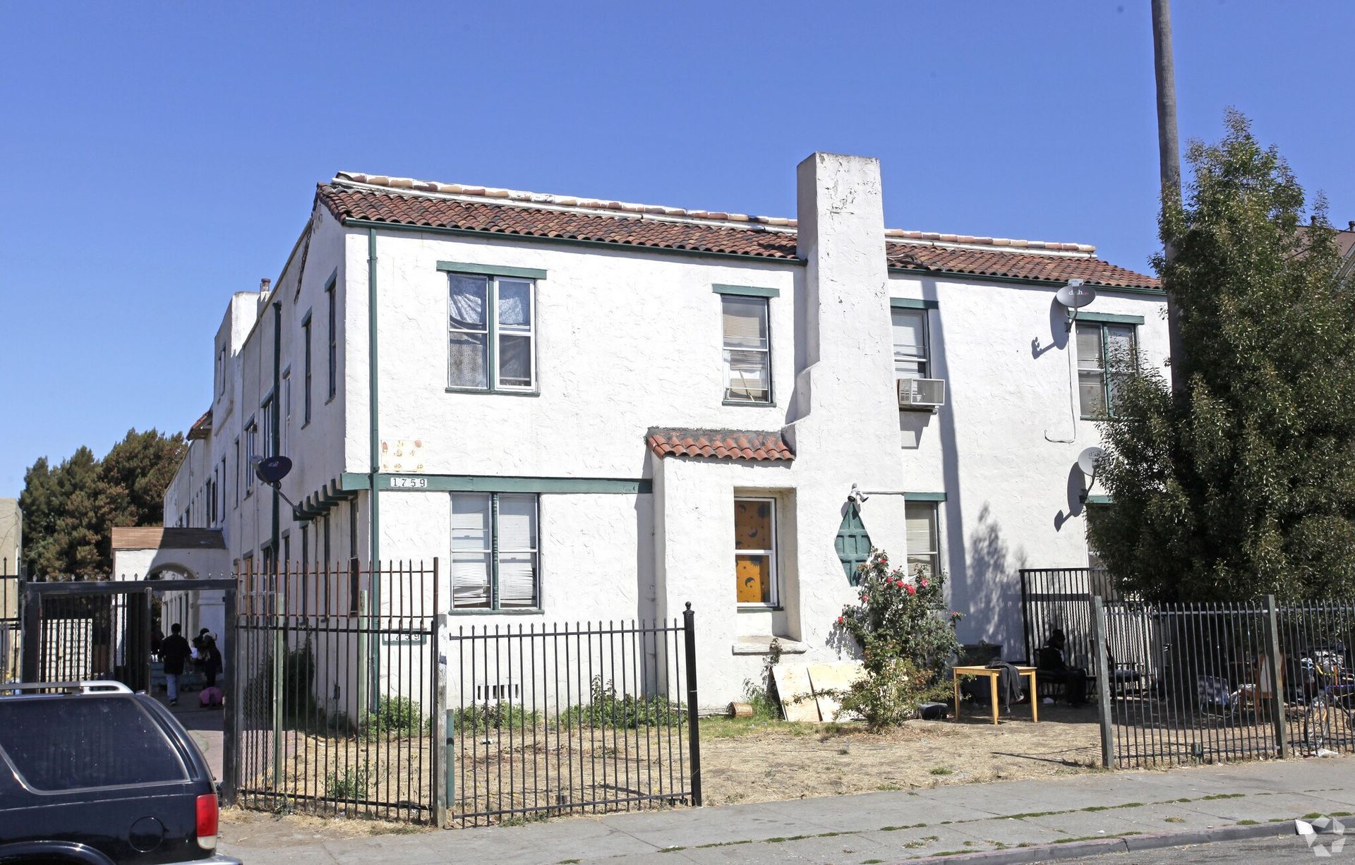 Two-story white stucco building with a red-tile roof and a small fenced yard.