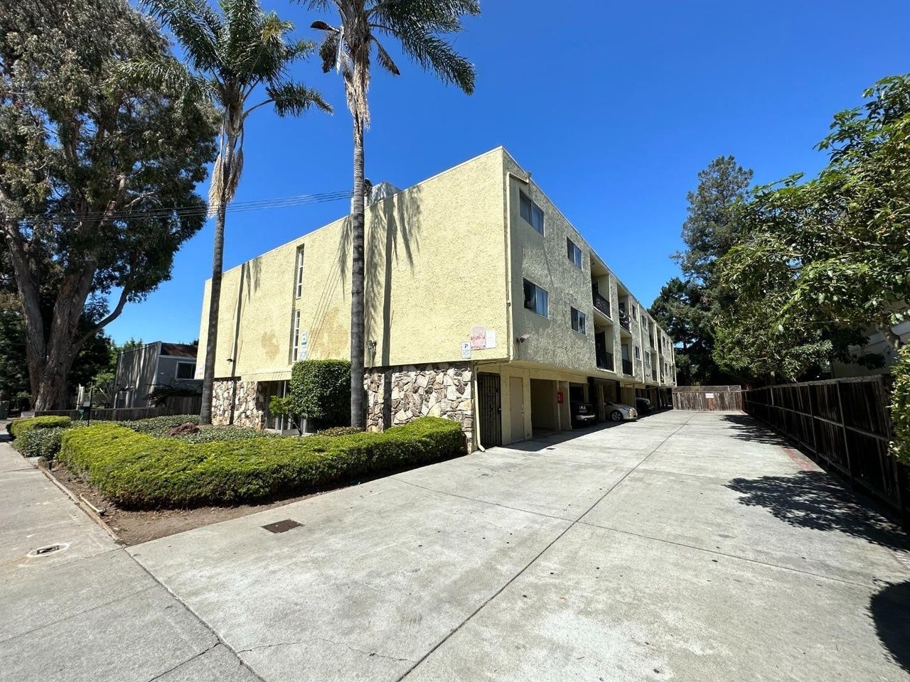 Yellow apartment building with stone facade, palm trees, and driveway.