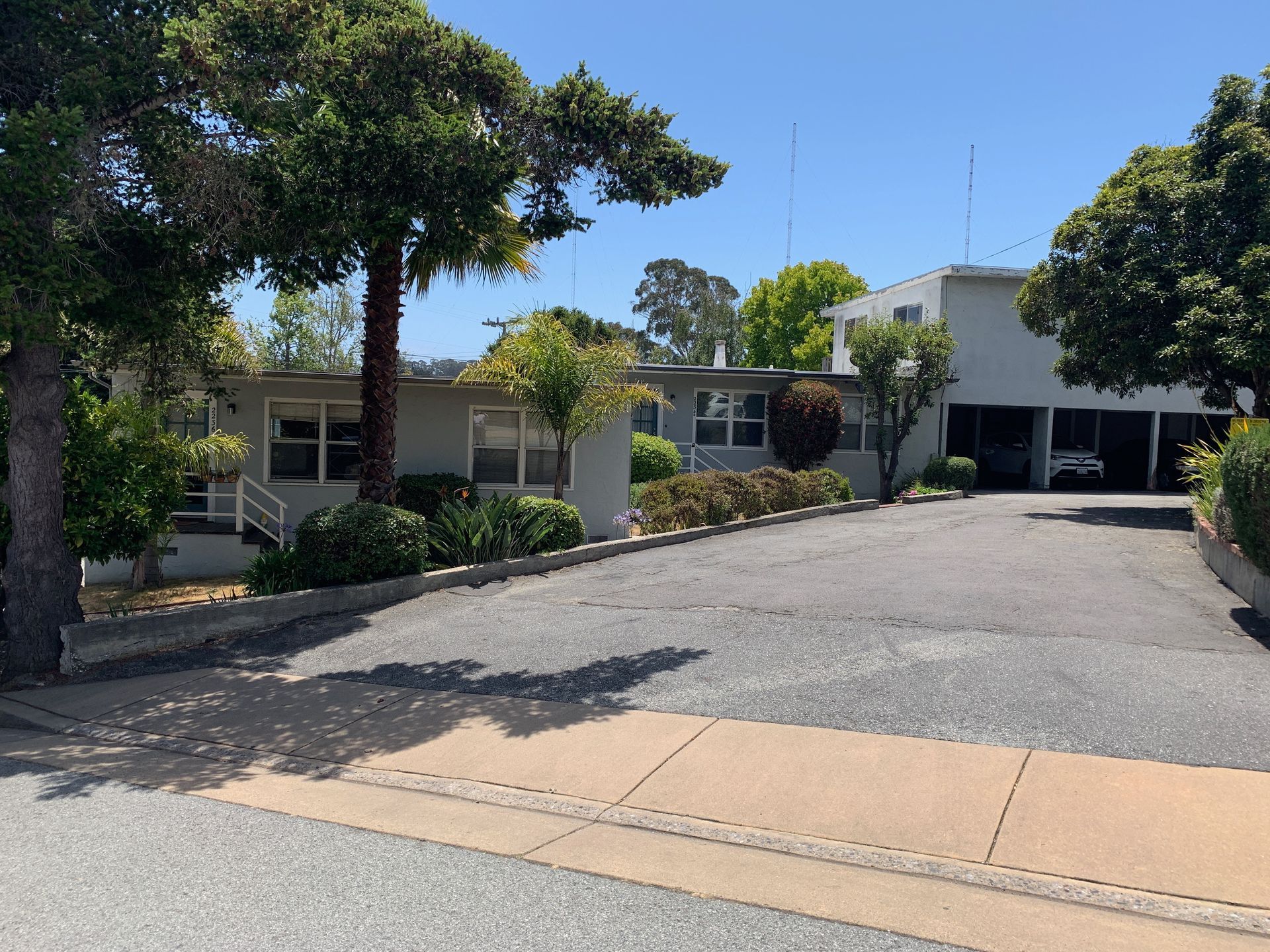 Gray house with driveway; trees and landscaping. Sunny day.