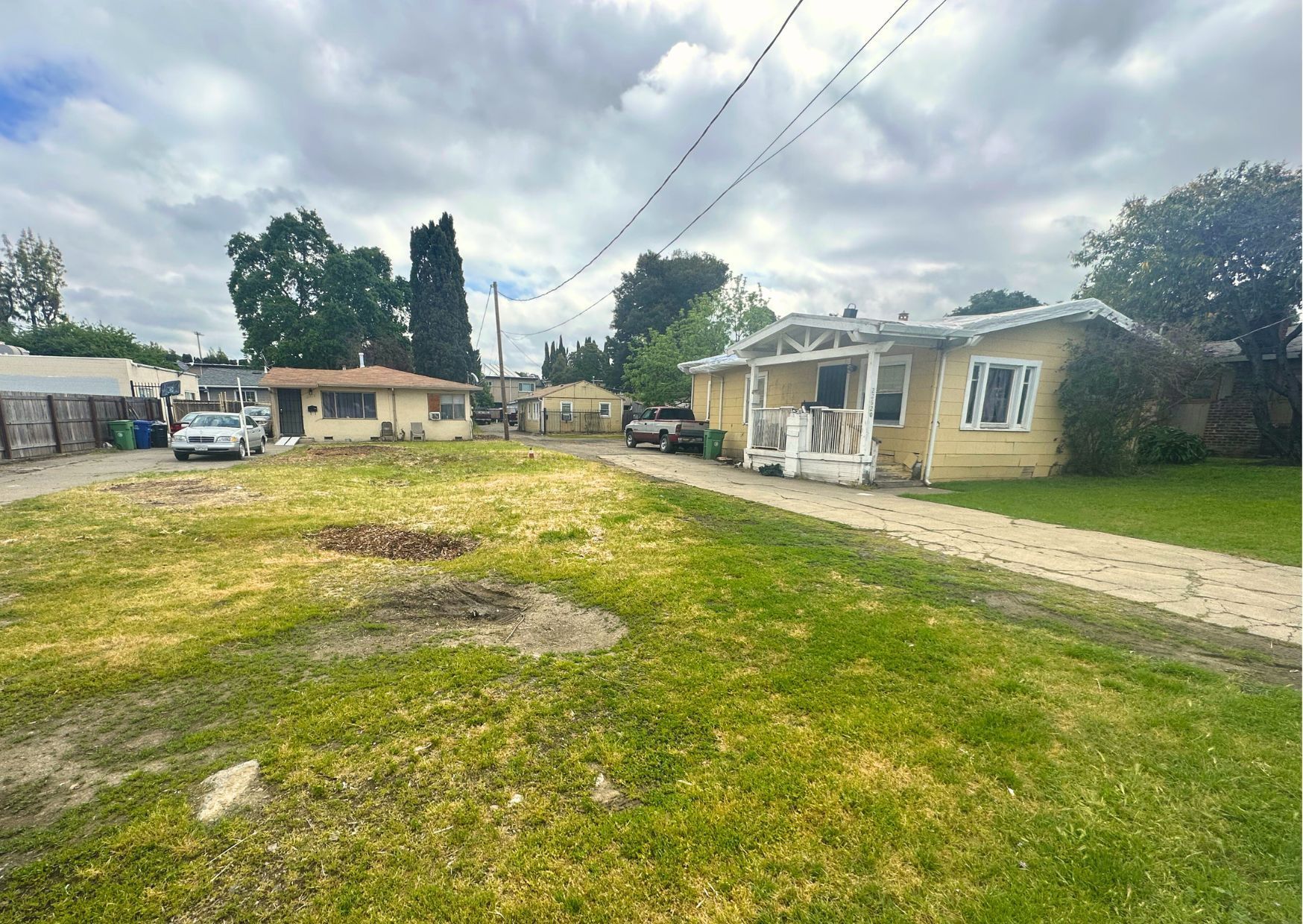 Grassy lot with two small, yellow houses under a cloudy sky. One has a porch.