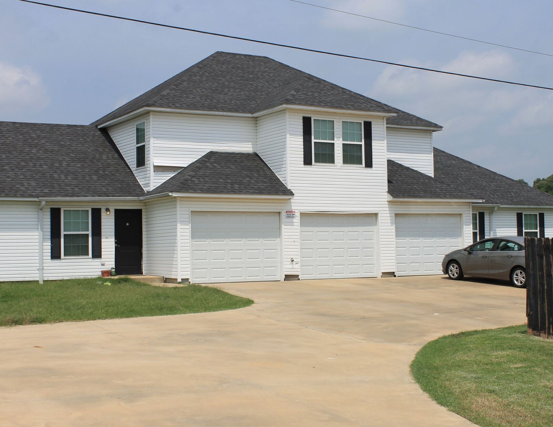 White multi-unit building with three attached garages, black shutters, and a driveway.