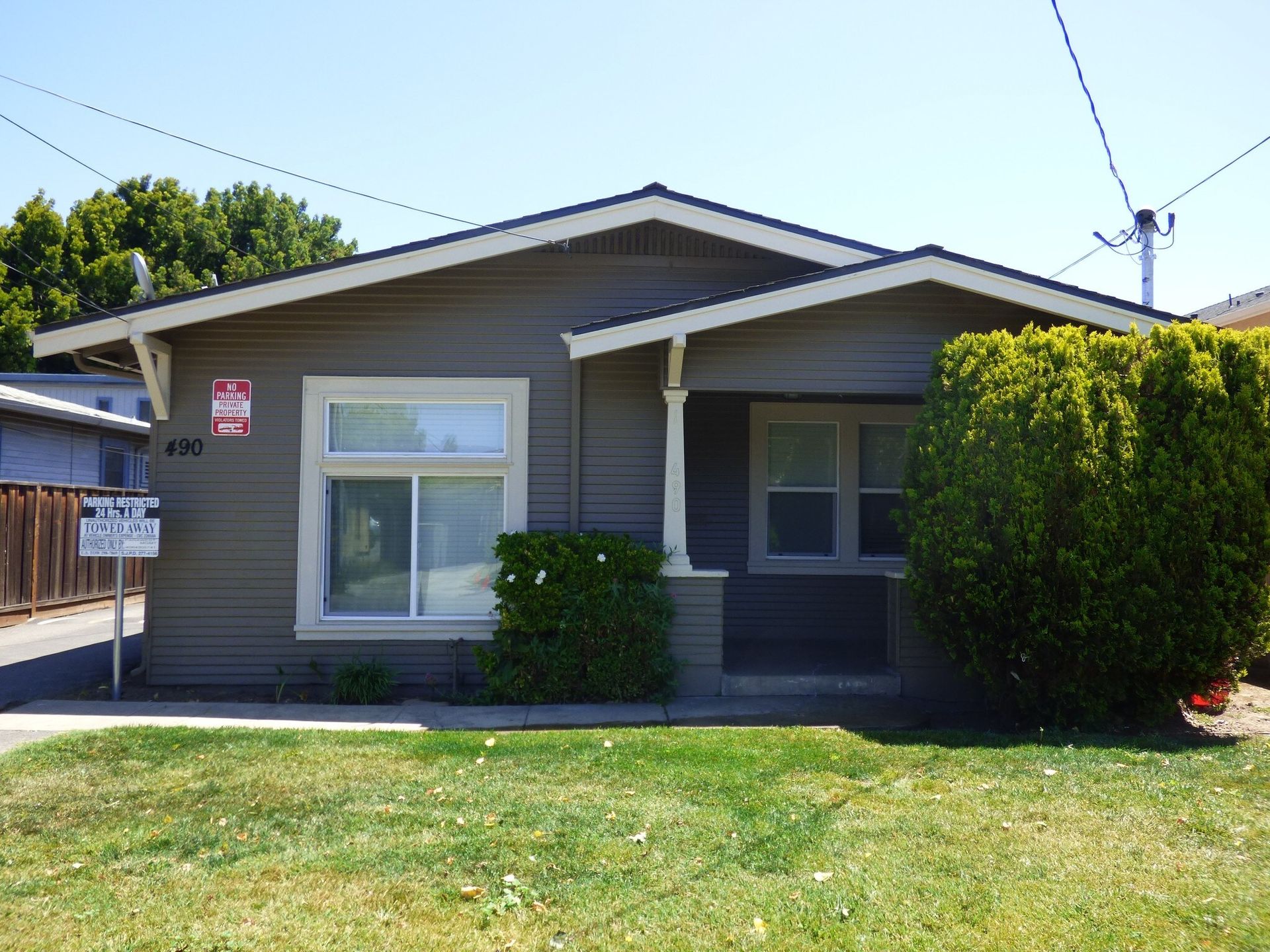Gray house with white window frames and small front porch, small green bush on the right, sunny day.