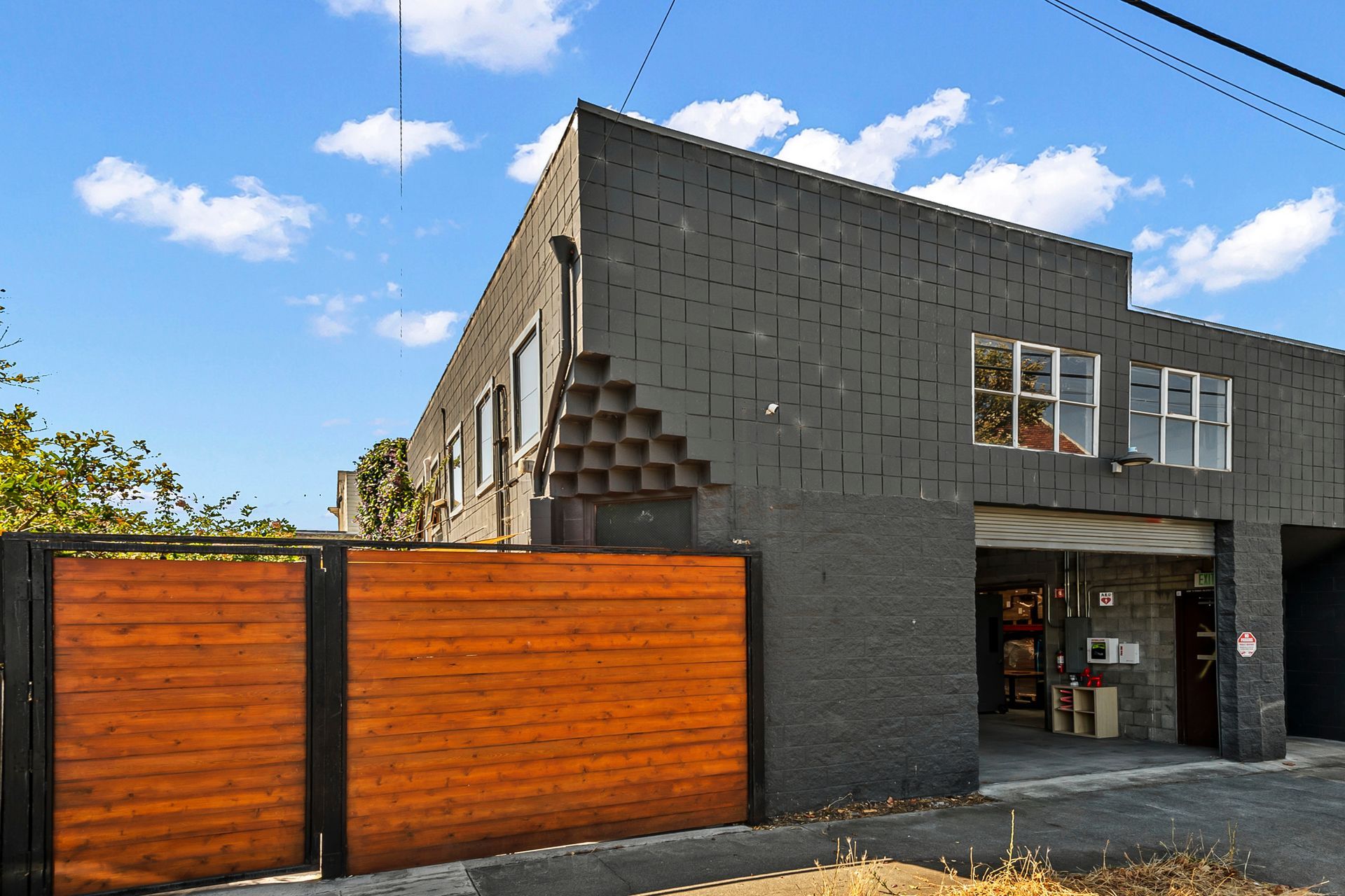 A dark gray commercial building with a wooden gate, blue sky.