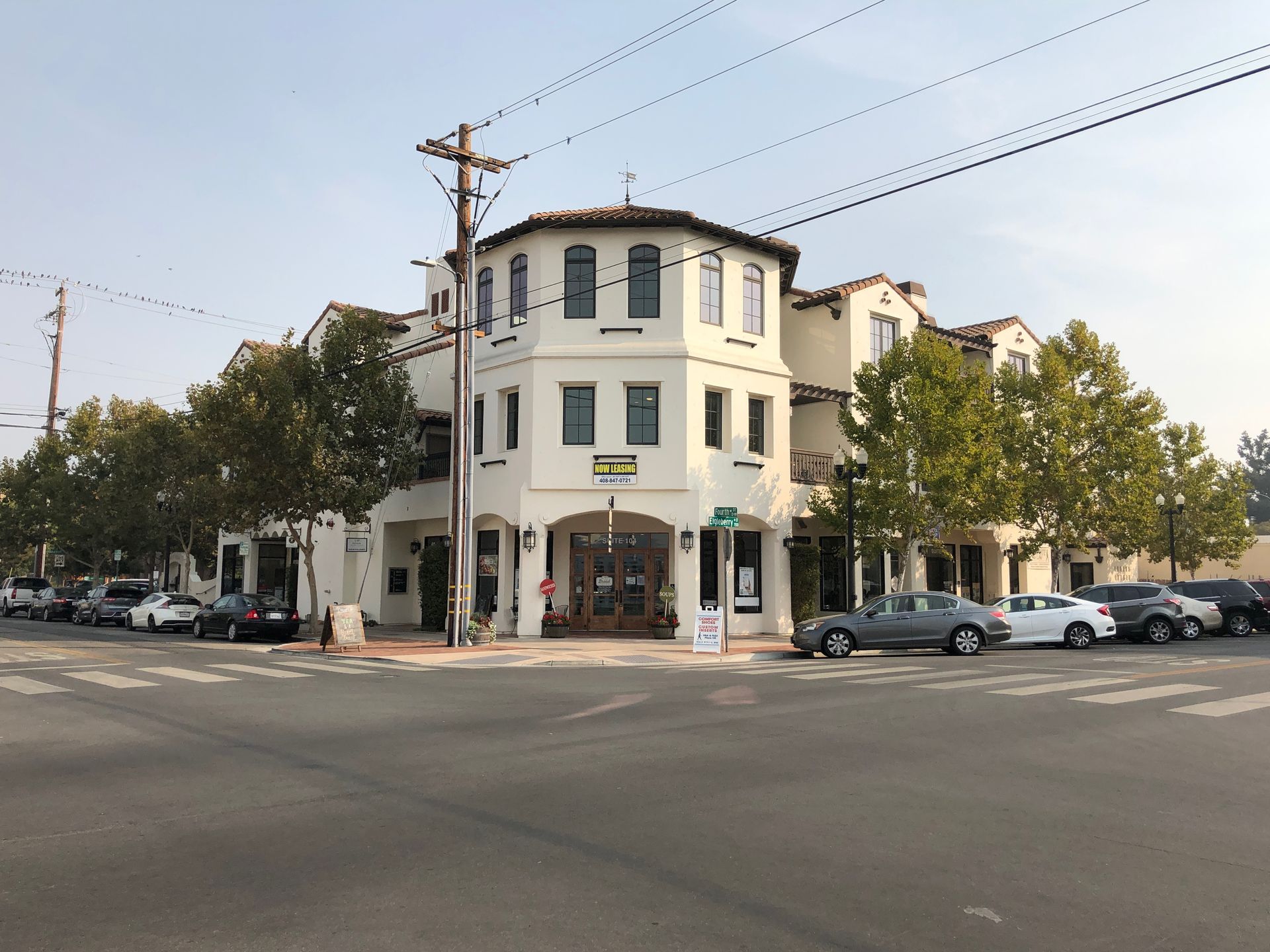 Corner building, tan exterior, multi-story, shops on ground floor, cars parked on street.